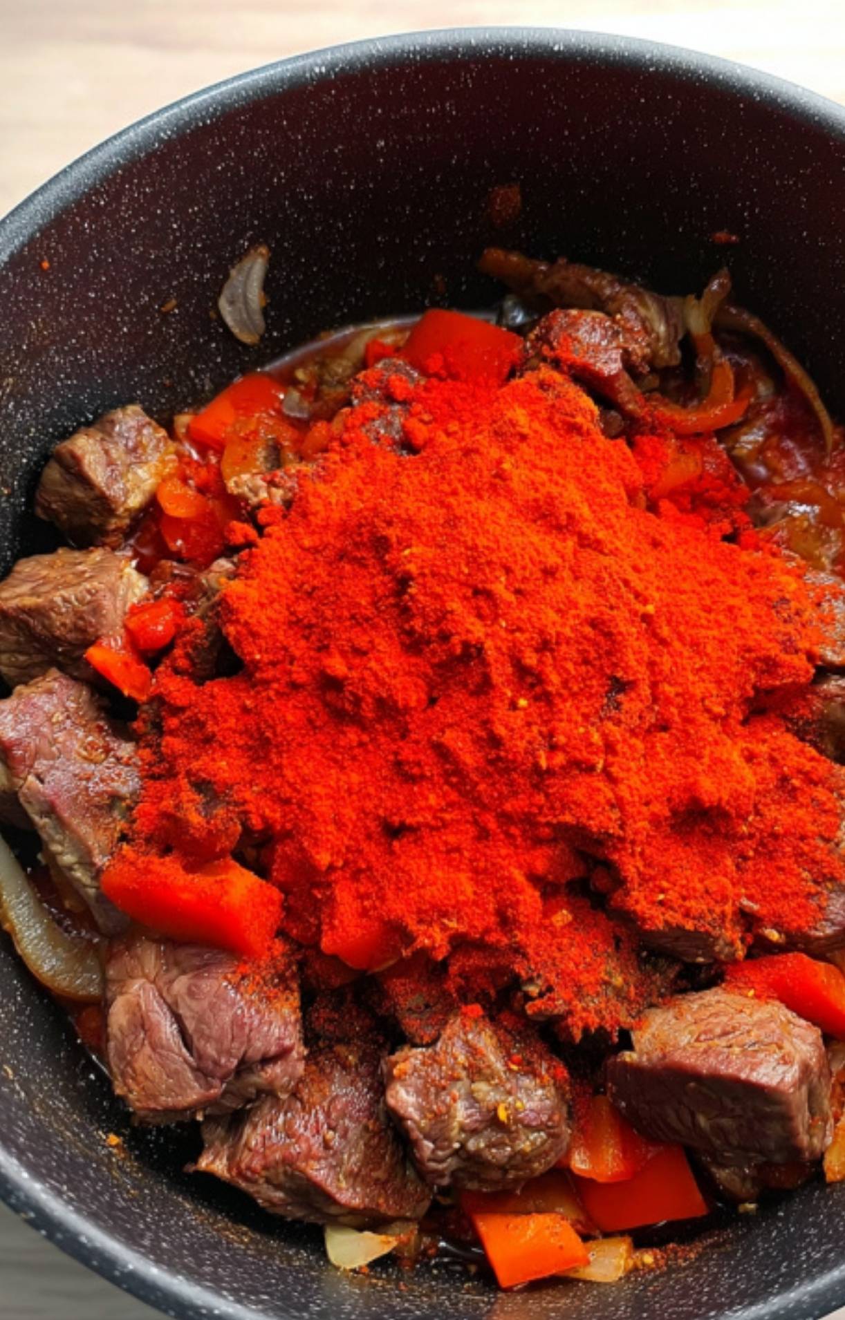 Generous spoonfuls of bright red Hungarian paprika covering beef, peppers, and onions in a pot. This is the secret to deep, rich goulash flavor.