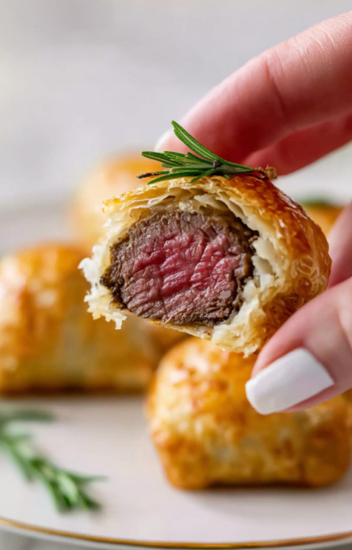 Hand holding a bite-sized Mini Beef Wellington with golden pastry and tender steak, a top choice for easy entertaining and holiday parties.