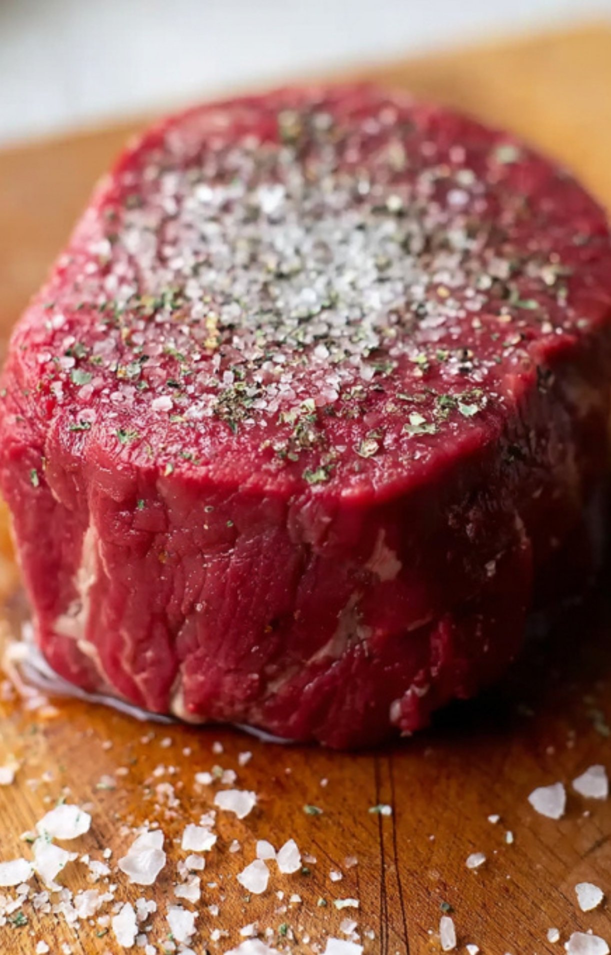 Close-up of raw filet mignon steak sprinkled with flaky sea salt and black pepper, ready for making beef Wellington.