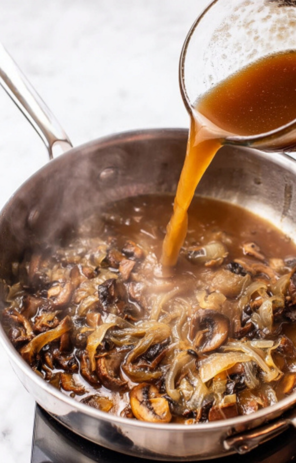Beef broth poured into a skillet of sautéed onions and mushrooms to create a savory, thick mushroom gravy for Salsberry Steak With Mushroom Gravy.