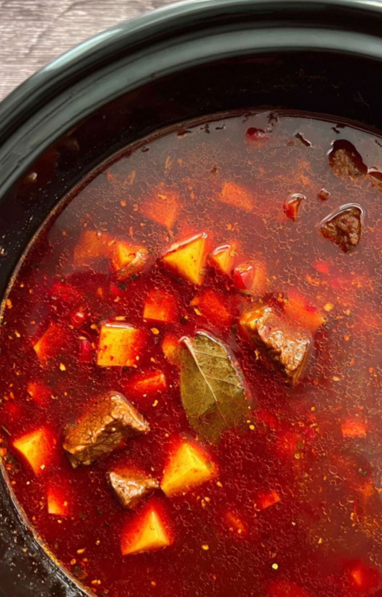 Goulash simmering in the slow cooker, loaded with potatoes, beef, carrots, and a bay leaf for classic aroma. Brothy, vibrant, and full of flavor.
