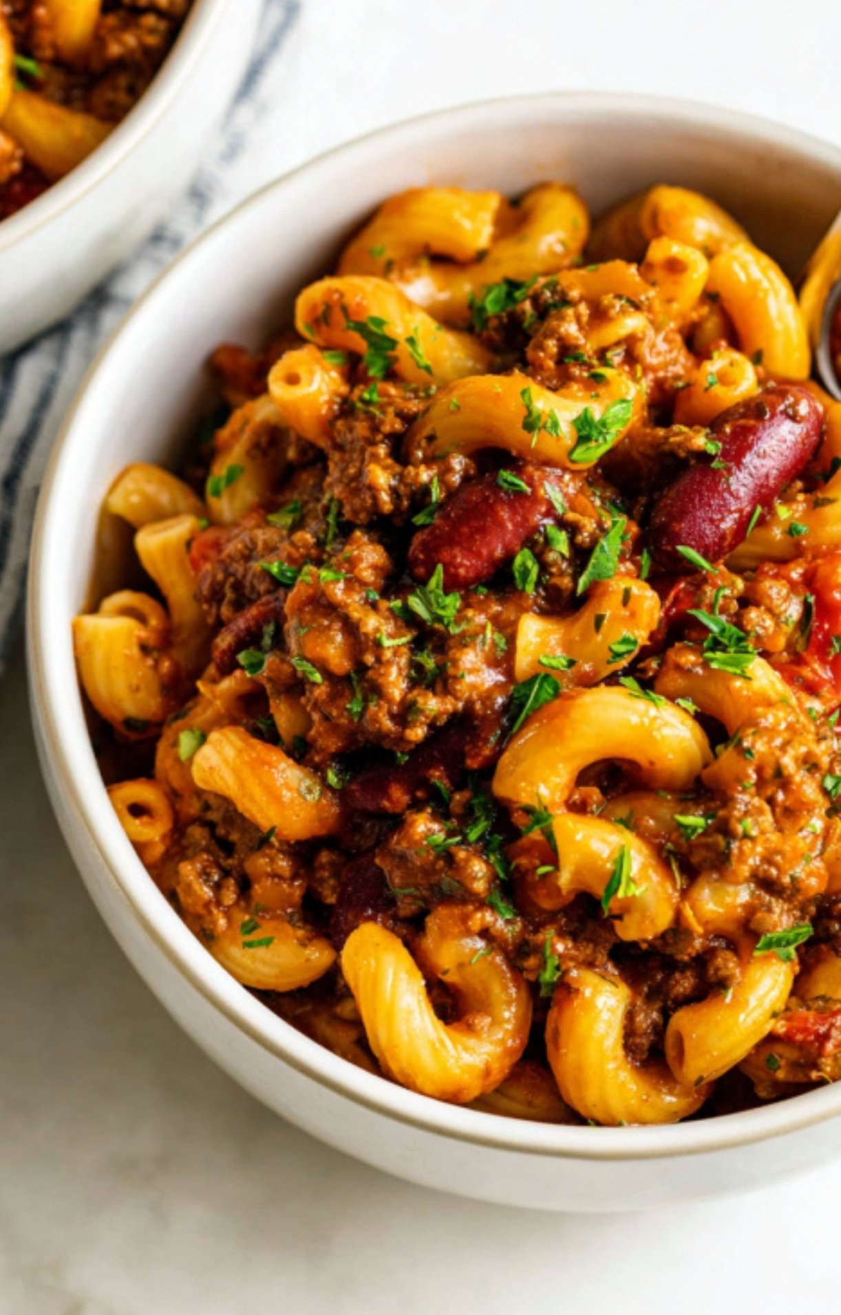 Bowl of American goulash with ground beef, elbow noodles, kidney beans, and chopped parsley on top. Cozy, cheesy, and ready to eat for a quick family meal.