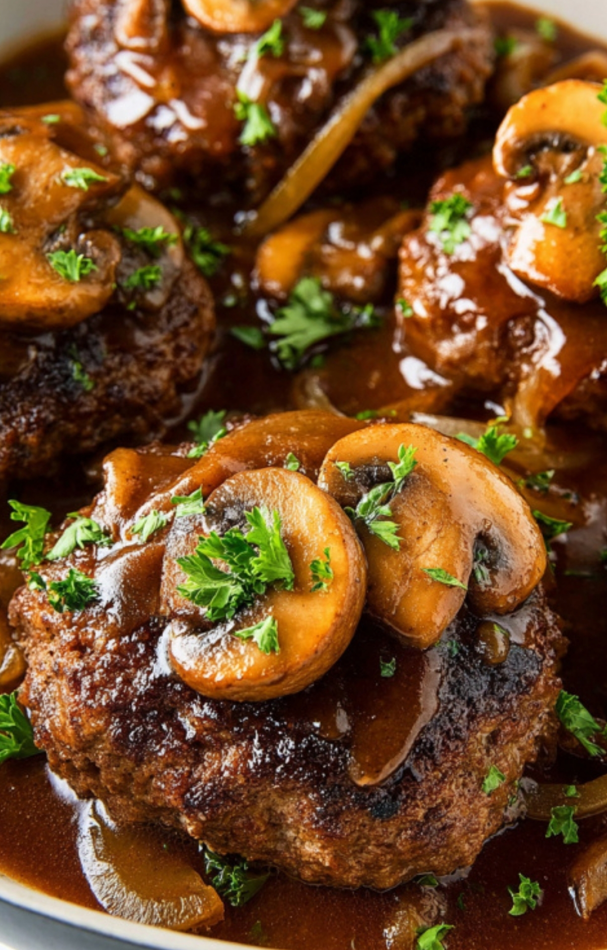 Close-up of Salisbury steak patty smothered in brown gravy with sliced mushrooms and fresh parsley.