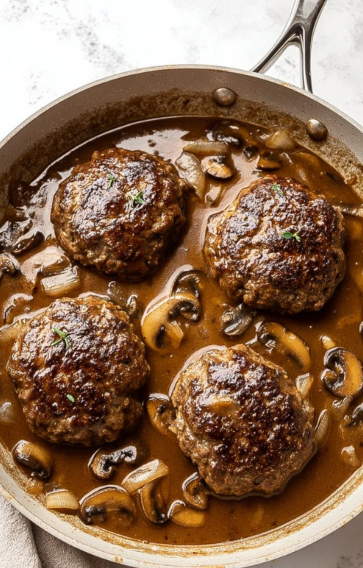 Beef patties simmering in rich mushroom and onion gravy in a skillet—a hearty Salsberry Steak recipe, perfect for weeknight comfort meals and family dinners.