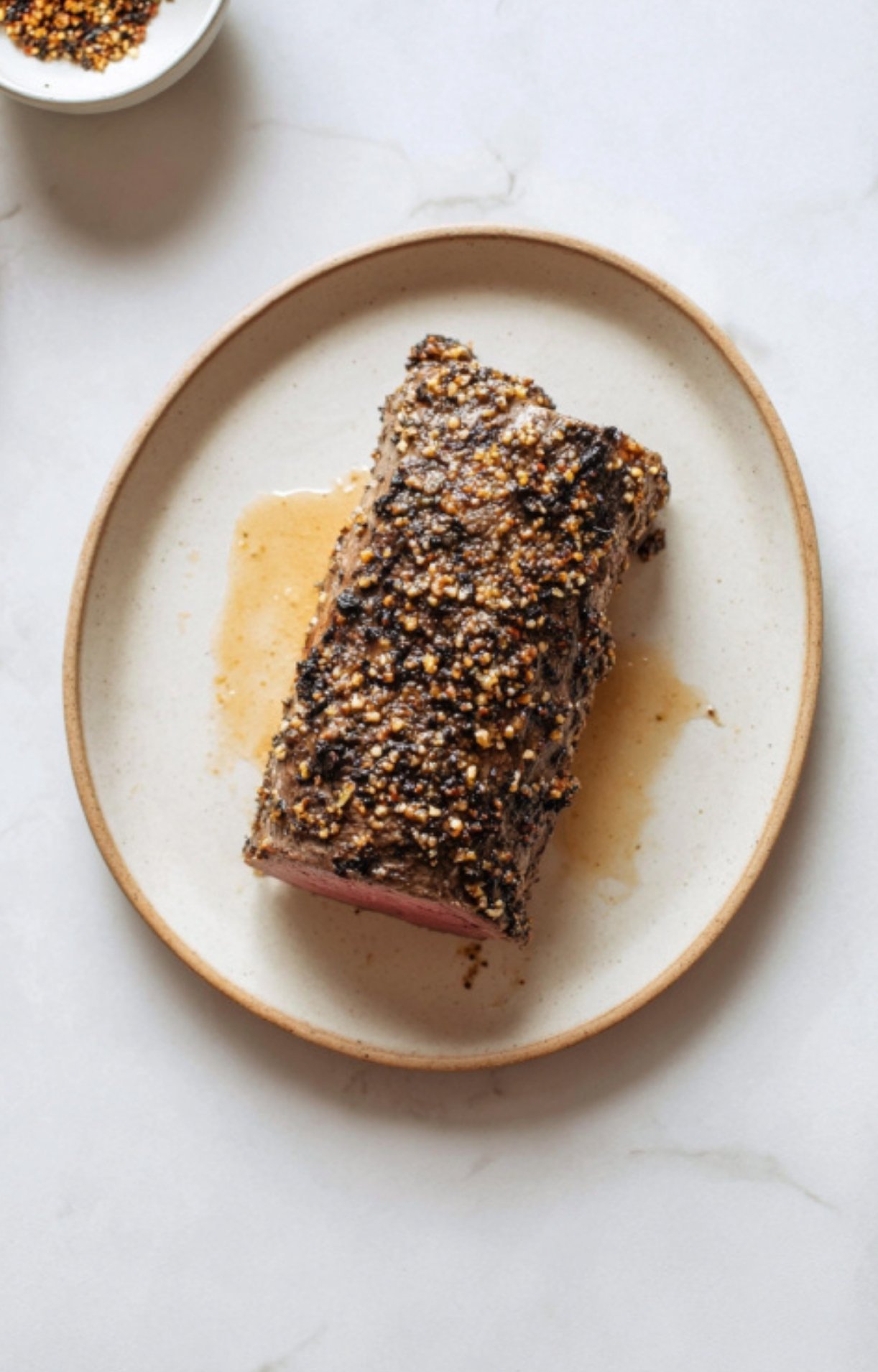 Seared beef tenderloin coated with mustard and spices on a plate, the key step for making beef wellington without mushrooms for holidays or family celebrations