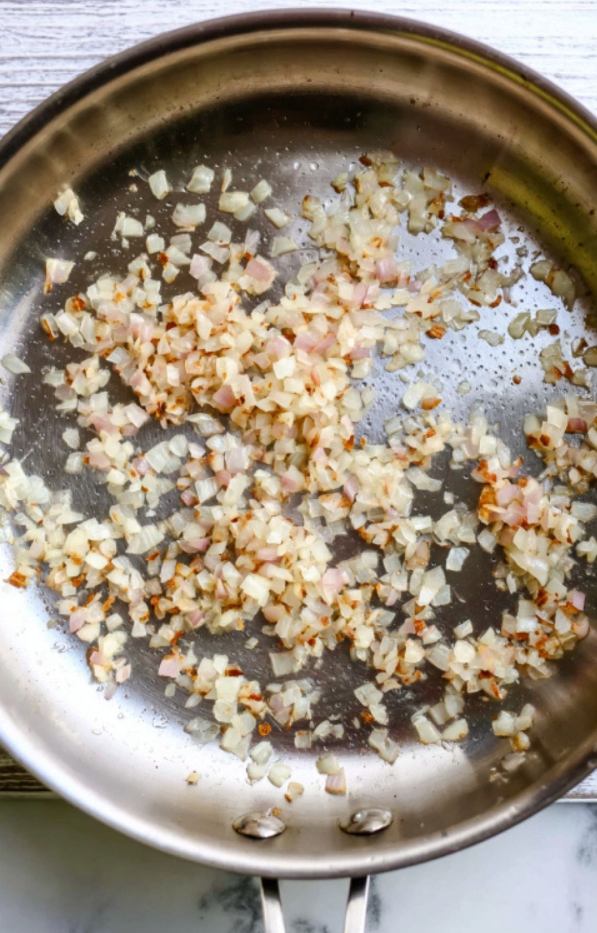 Chopped shallots sautéed in a pan, building the flavor base for classic beef wellington red wine sauce.