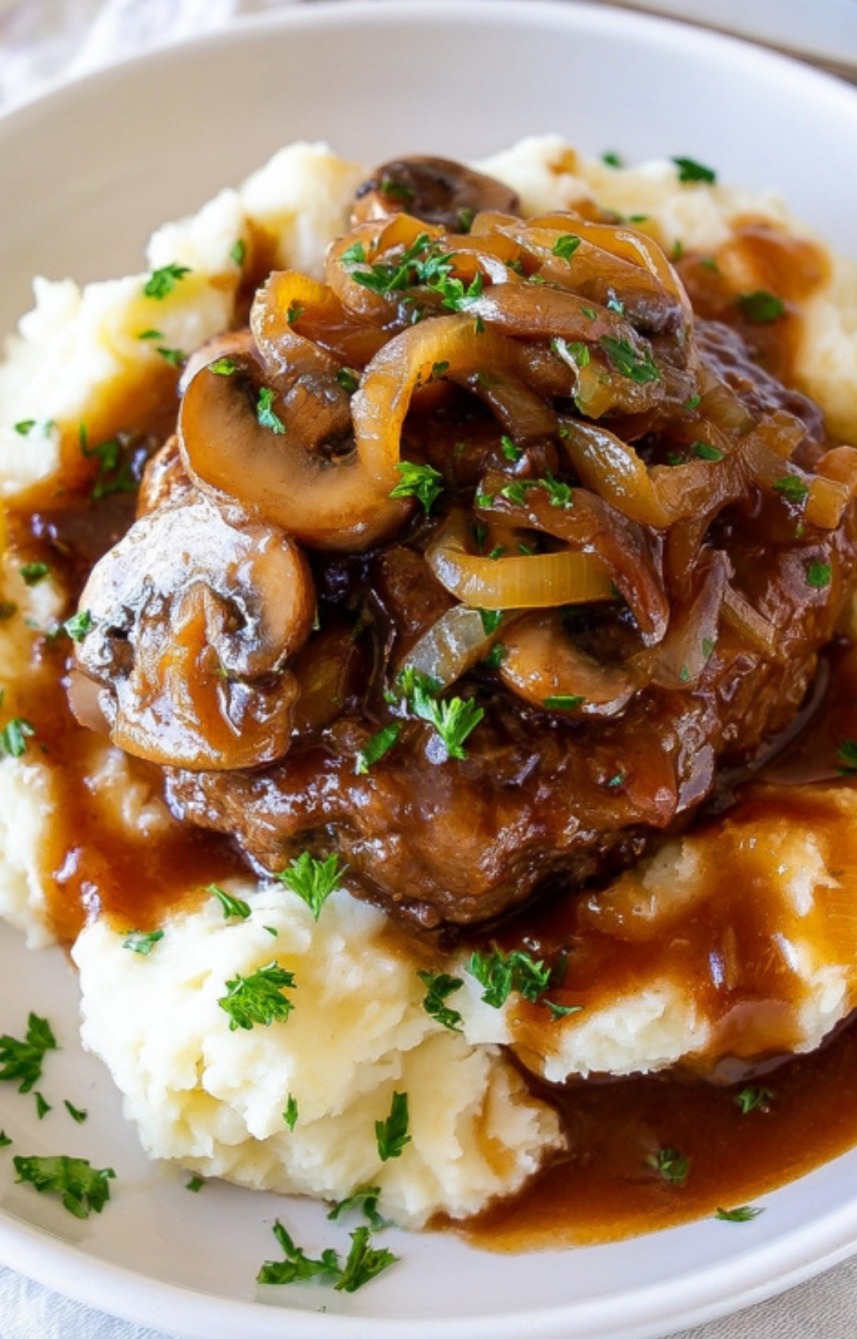 Tender Salisbury steak topped with rich mushroom and onion gravy, served over fluffy mashed potatoes, garnished with fresh herbs.
