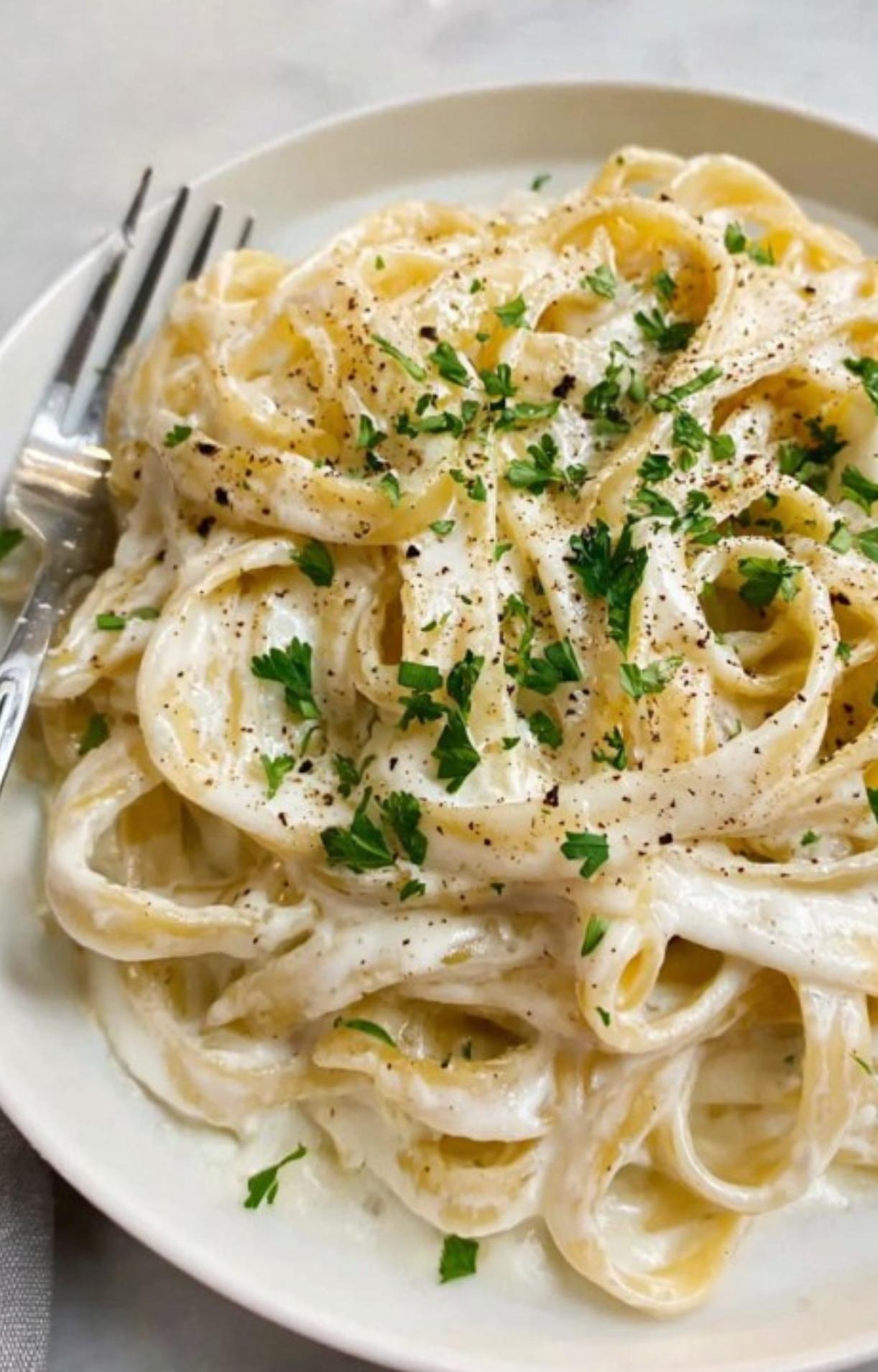 Close-up of creamy pasta in a white bowl, garnished with chopped parsley and cracked black pepper, ideal for quick weeknight meals.