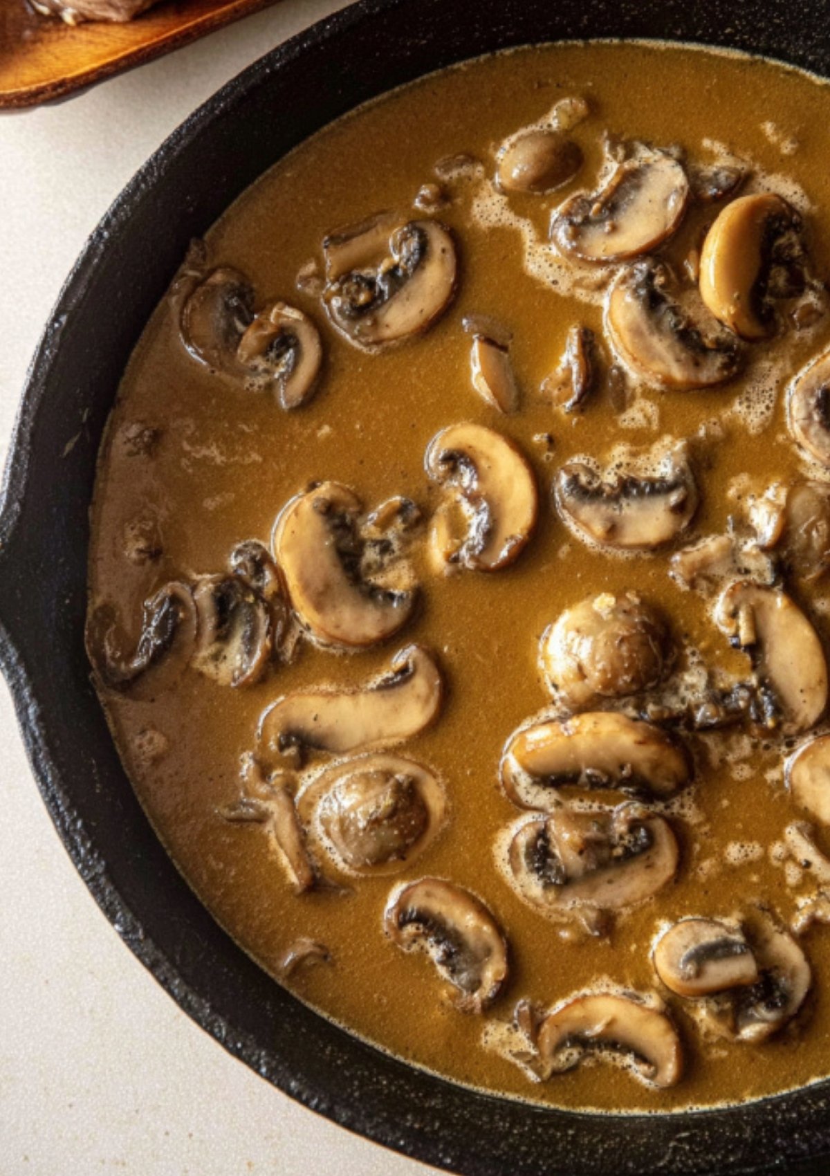 Golden brown mushroom gravy with sliced mushrooms and onions in a skillet.
