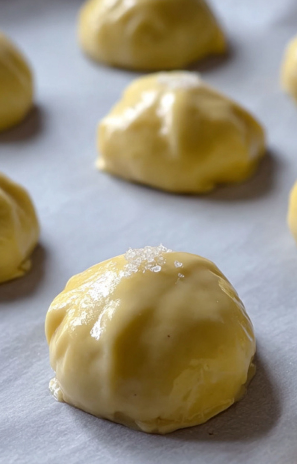 Unbaked Mini Beef Wellington parcels brushed with egg wash, ready for the oven to become golden appetizers for parties and special events.