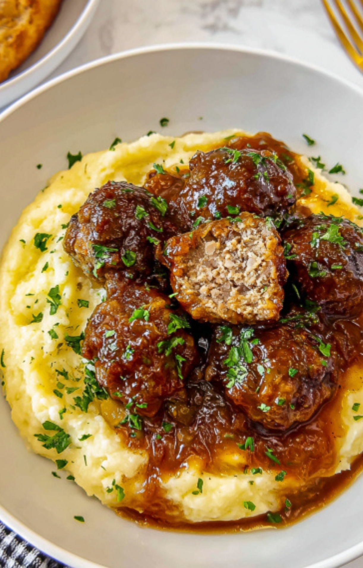 Bowl of mashed potatoes topped with Salisbury Steak Meatballs and savory gravy, garnished with parsley.