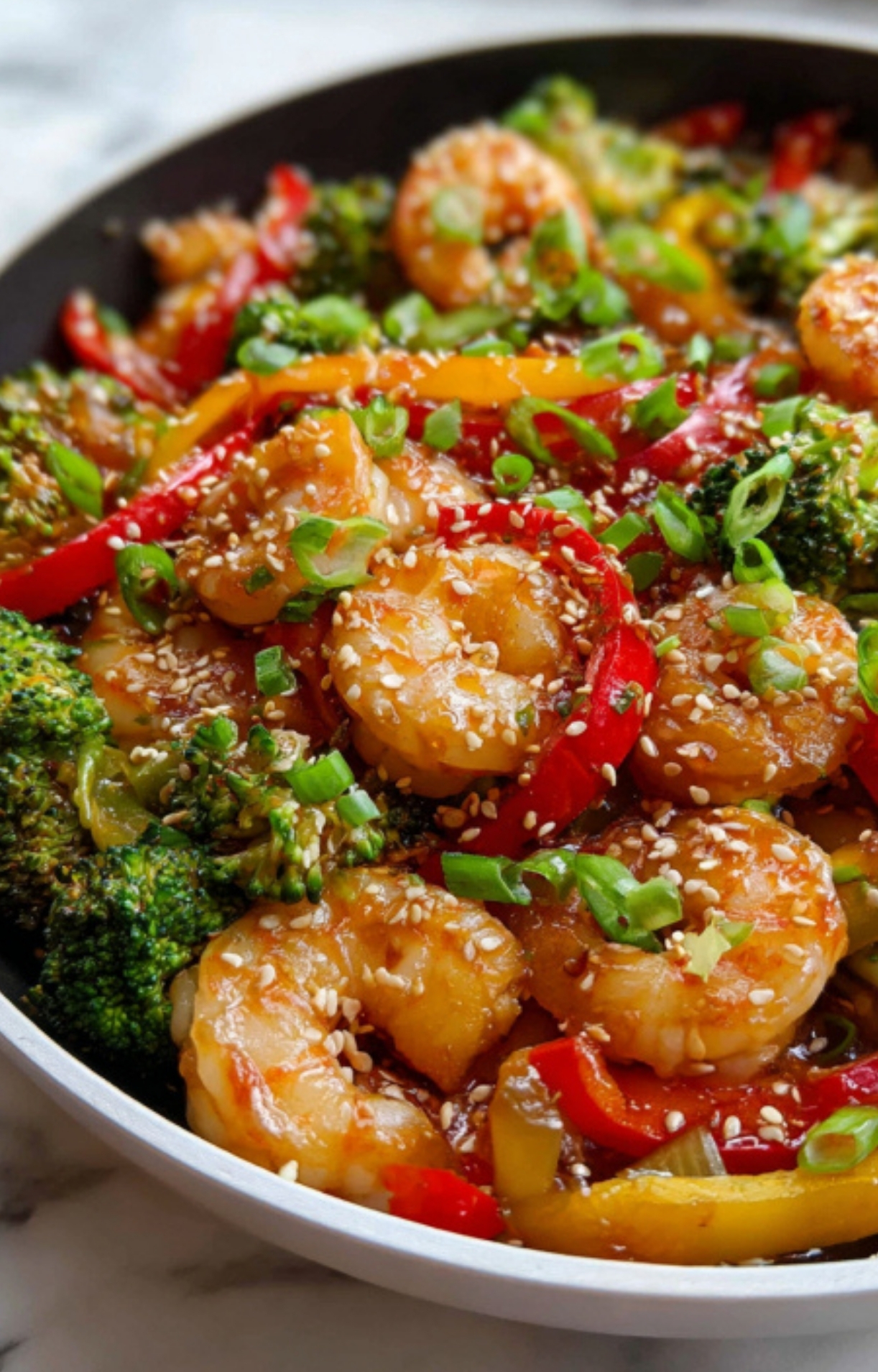 Close-up of shrimp stir-fry with broccoli, red and yellow peppers, green onions, and sesame seeds in a bowl – fast healthy dinner recipe