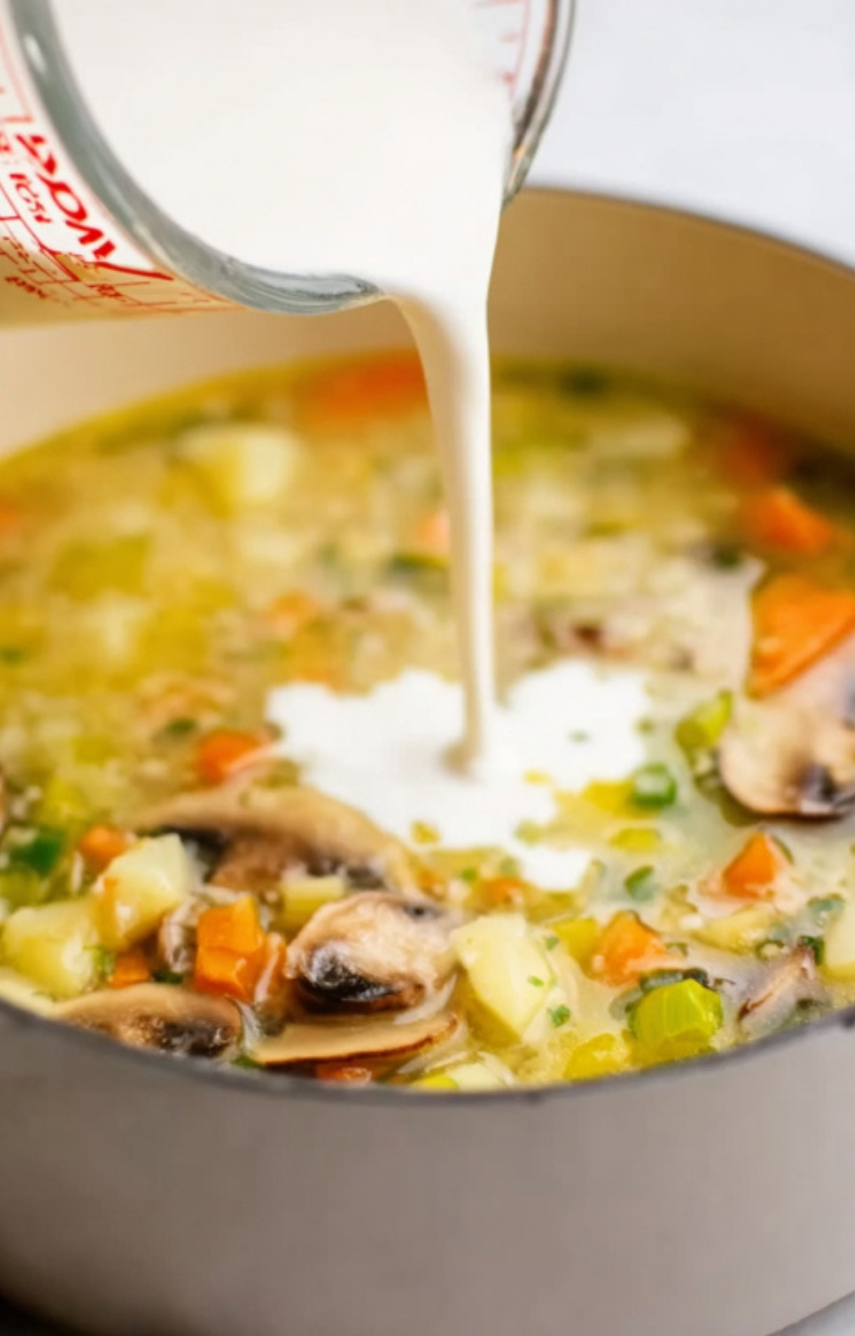 A saucepan of creamy French vegetable soup with cream being poured in, showing the rich, comforting texture. Perfect for cozy spring dinners and family gatherings.