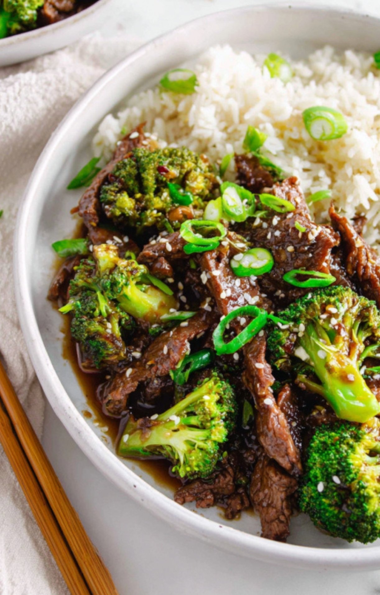 Bowl of shaved beef and broccoli stir fry served over fluffy rice, topped with sliced green onions and sesame seeds for a quick and healthy family dinner.