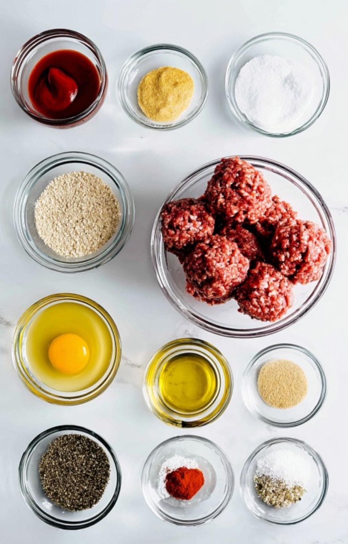 Ingredients for Salisbury Steak Meatballs arranged in glass bowls: ground beef, breadcrumbs, egg, oil, spices, and ketchup.