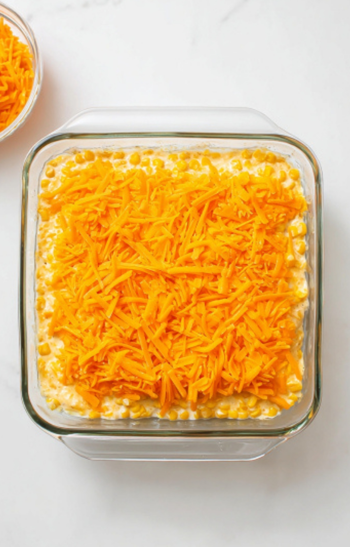 Unbaked cream cheese corn casserole topped with sharp cheddar cheese, ready to go in the oven for Thanksgiving, Christmas, or any potluck dinner.