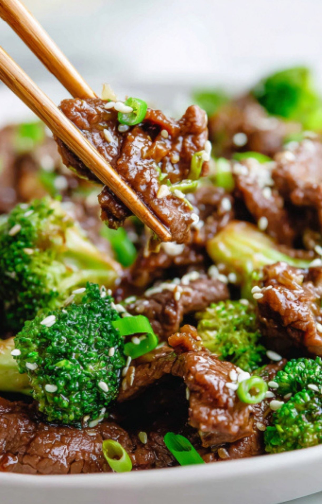 Chopsticks holding a bite of juicy shaved beef and broccoli, coated in savory sauce and sprinkled with sesame seeds, perfect for high protein weeknight meals.
