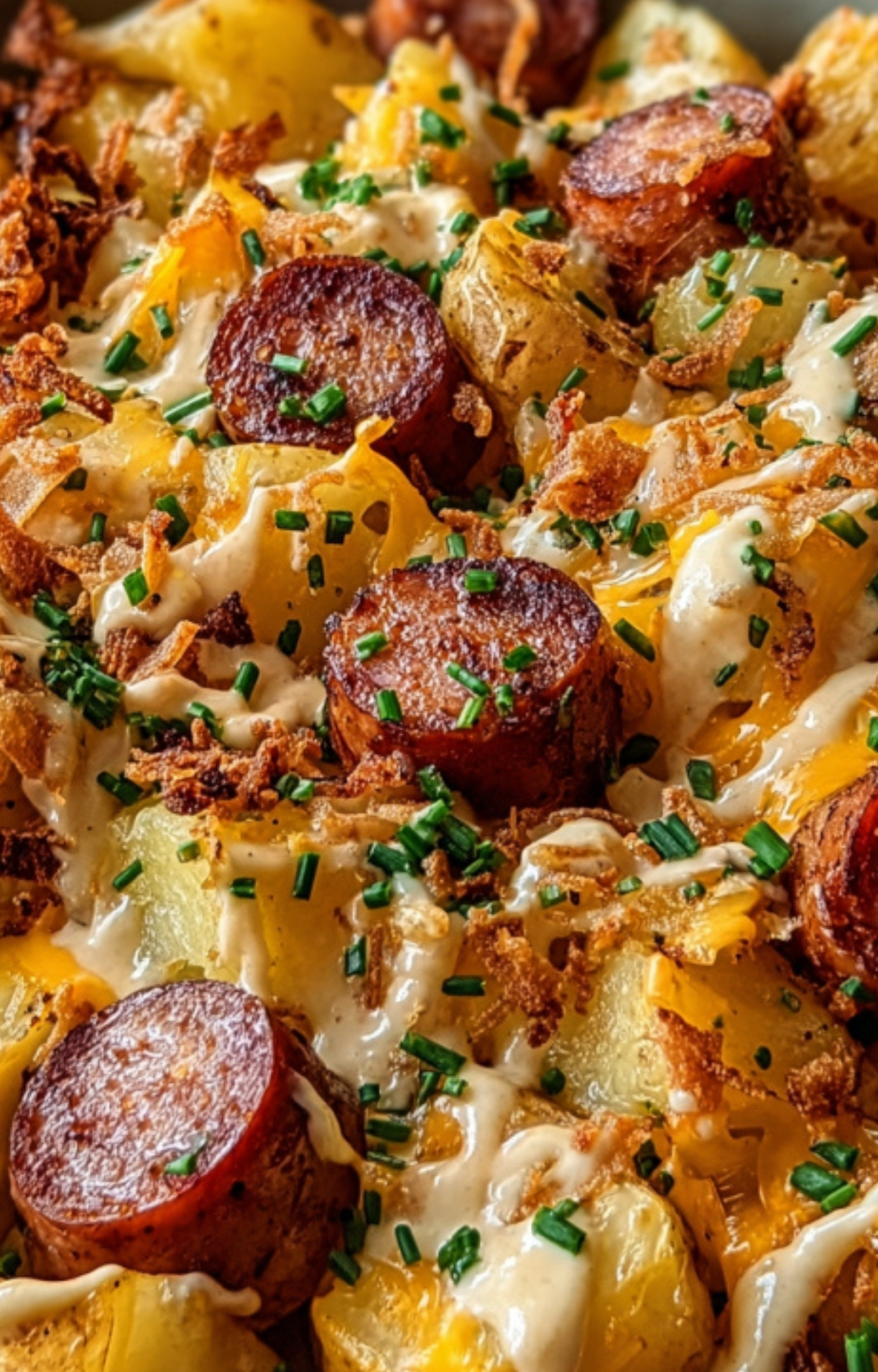 Close-up of golden roasted potatoes with sausage, melted cheddar cheese, ranch dressing, and fresh chives. Perfect for an easy family dinner or cozy holiday meal.