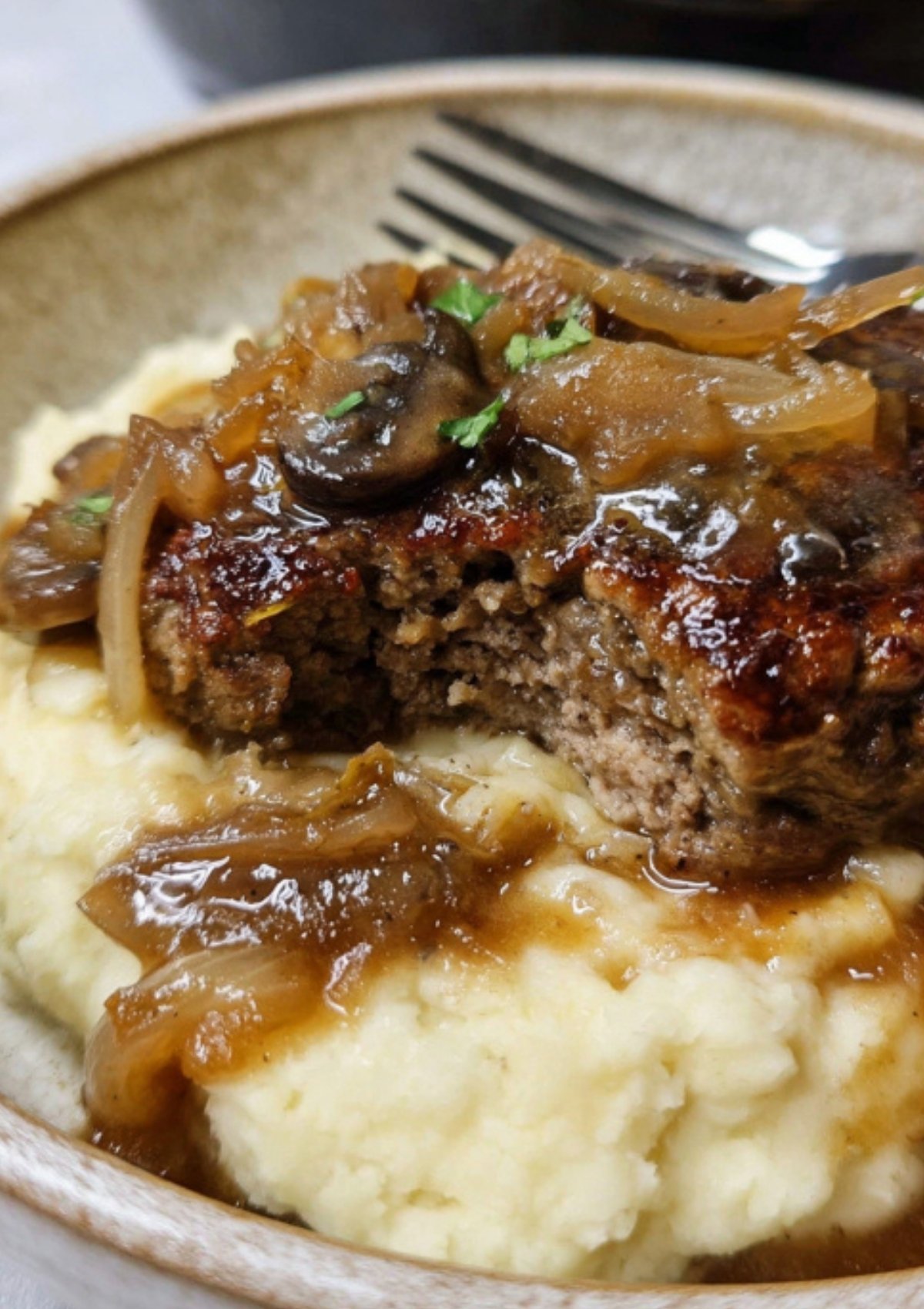 Juicy chop steak topped with savory mushroom onion gravy served over creamy mashed potatoes in a bowl.