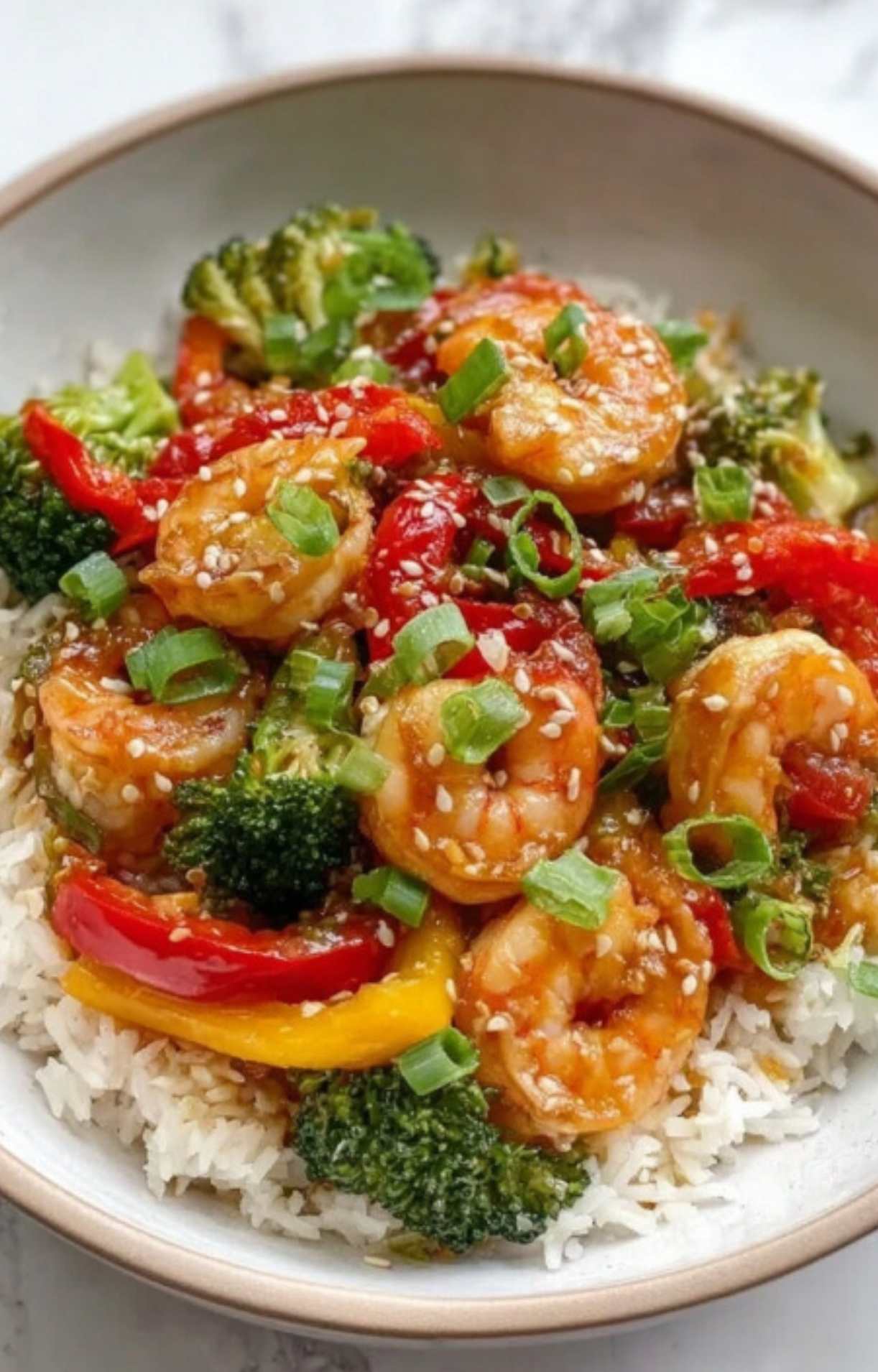 Bowl of shrimp stir-fry served over white rice with broccoli, red and yellow bell peppers, green onions, and sesame seeds – healthy dinner recipe
