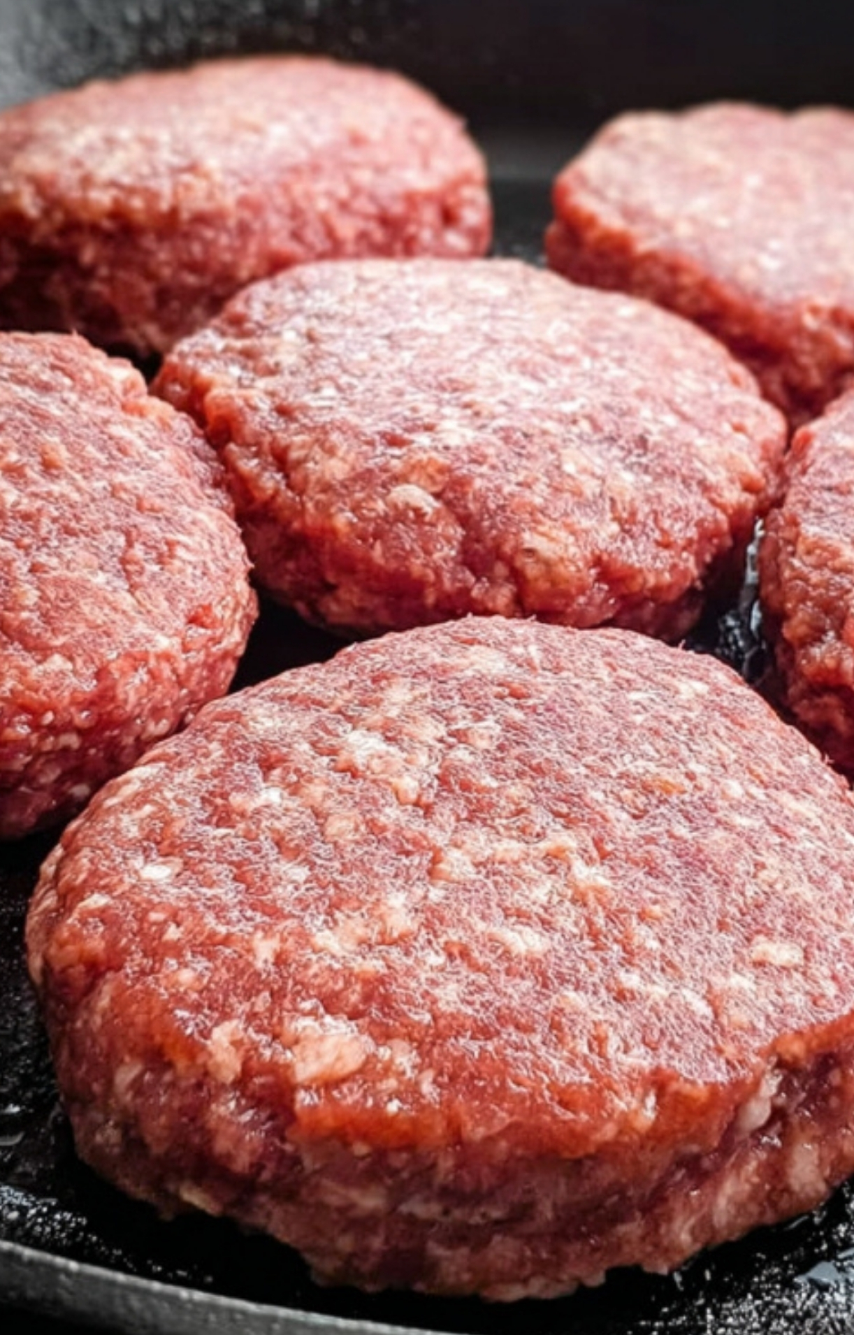 Freshly formed ground beef patties in a cast iron skillet, prepped for cooking traditional Salisbury steak.