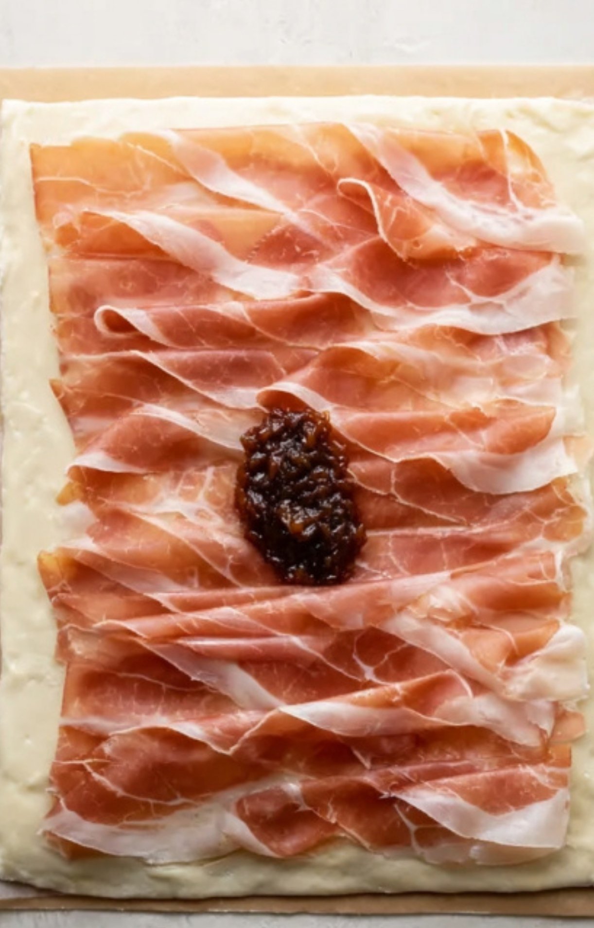 Puff pastry topped with layers of prosciutto and savory onion mixture, ready to wrap beef tenderloin for a holiday showstopper without mushrooms