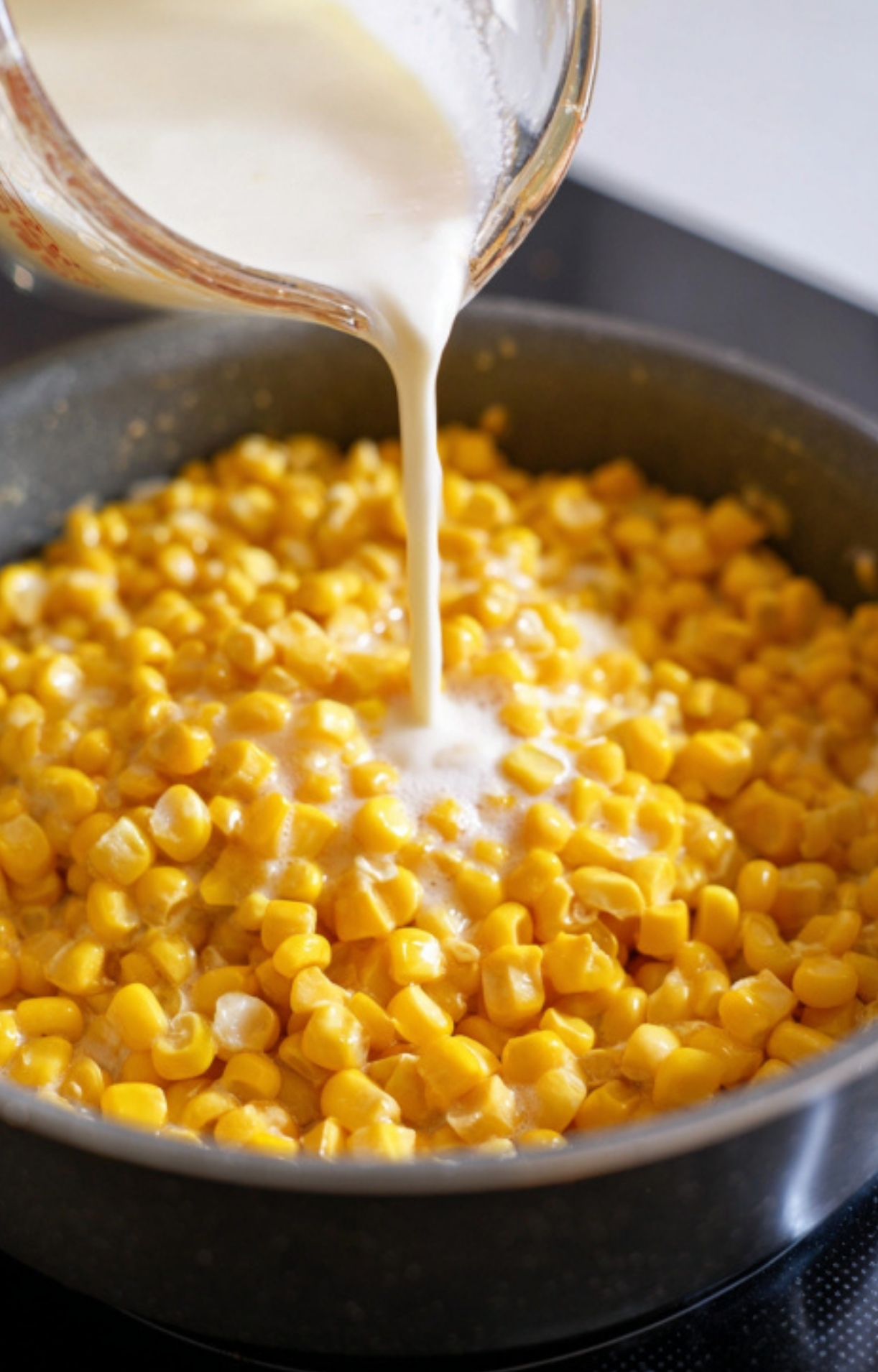 Cream being poured over canned corn kernels in a skillet, showing the start of a creamy Southern-style corn side dish, ideal for Thanksgiving or Christmas.