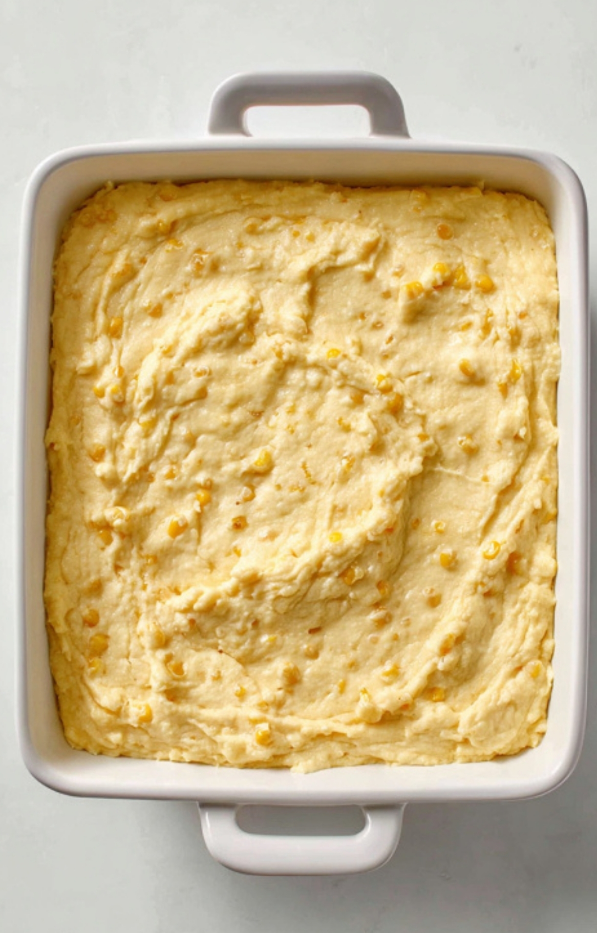 Unbaked corn pudding casserole batter in a white baking dish, ready for the oven. Perfect for Thanksgiving, Christmas, or any family dinner.