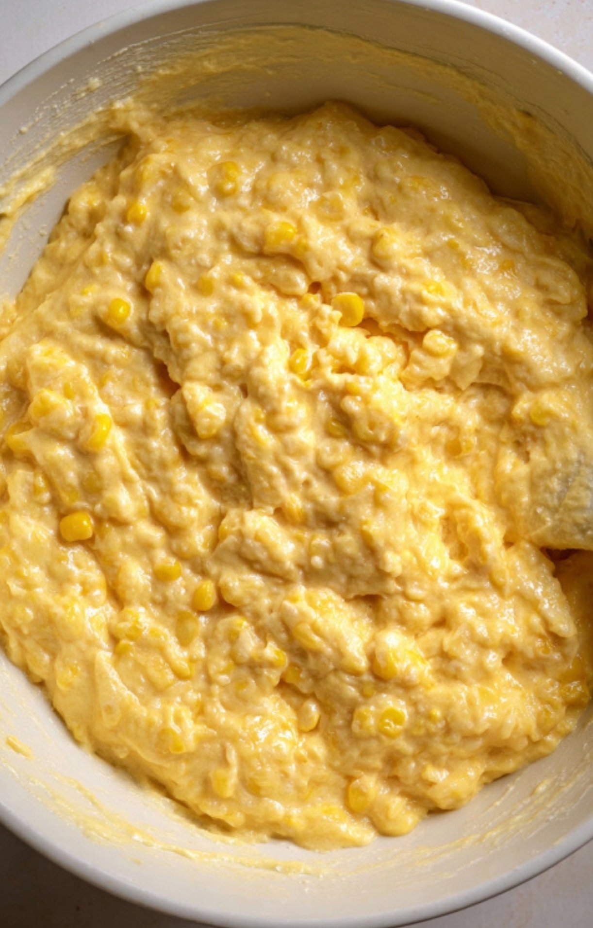 Mixing bowl filled with creamy corn pudding batter, showing fresh corn kernels and thick, rich texture. Step-by-step prep for classic holiday side dishes.