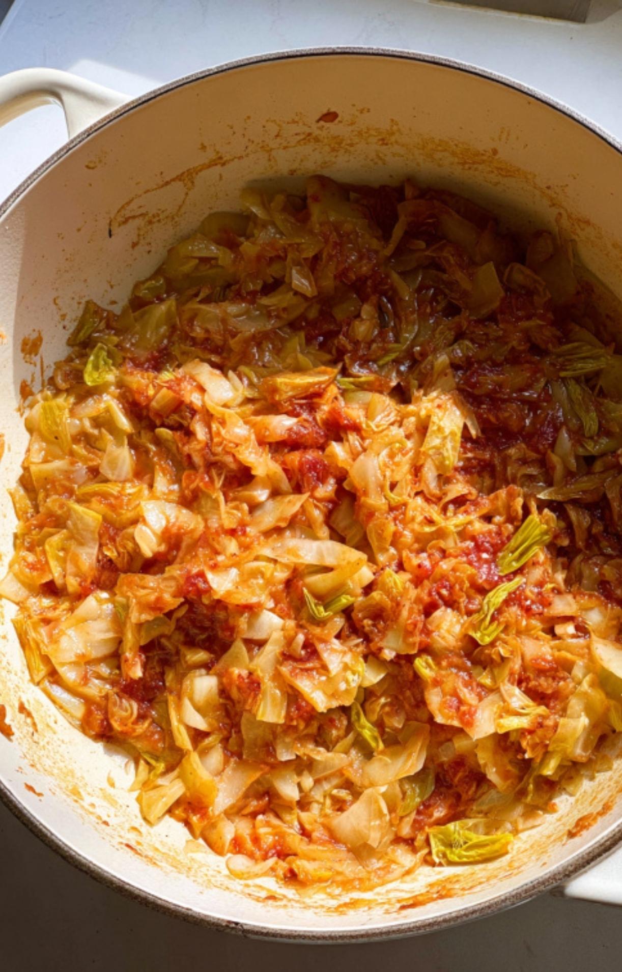 Dutch oven with sautéed cabbage and tomatoes, the hearty vegetable base for homemade bouillabaisse. Great for adding flavor and nutrition to winter stews and one-pot dinners.