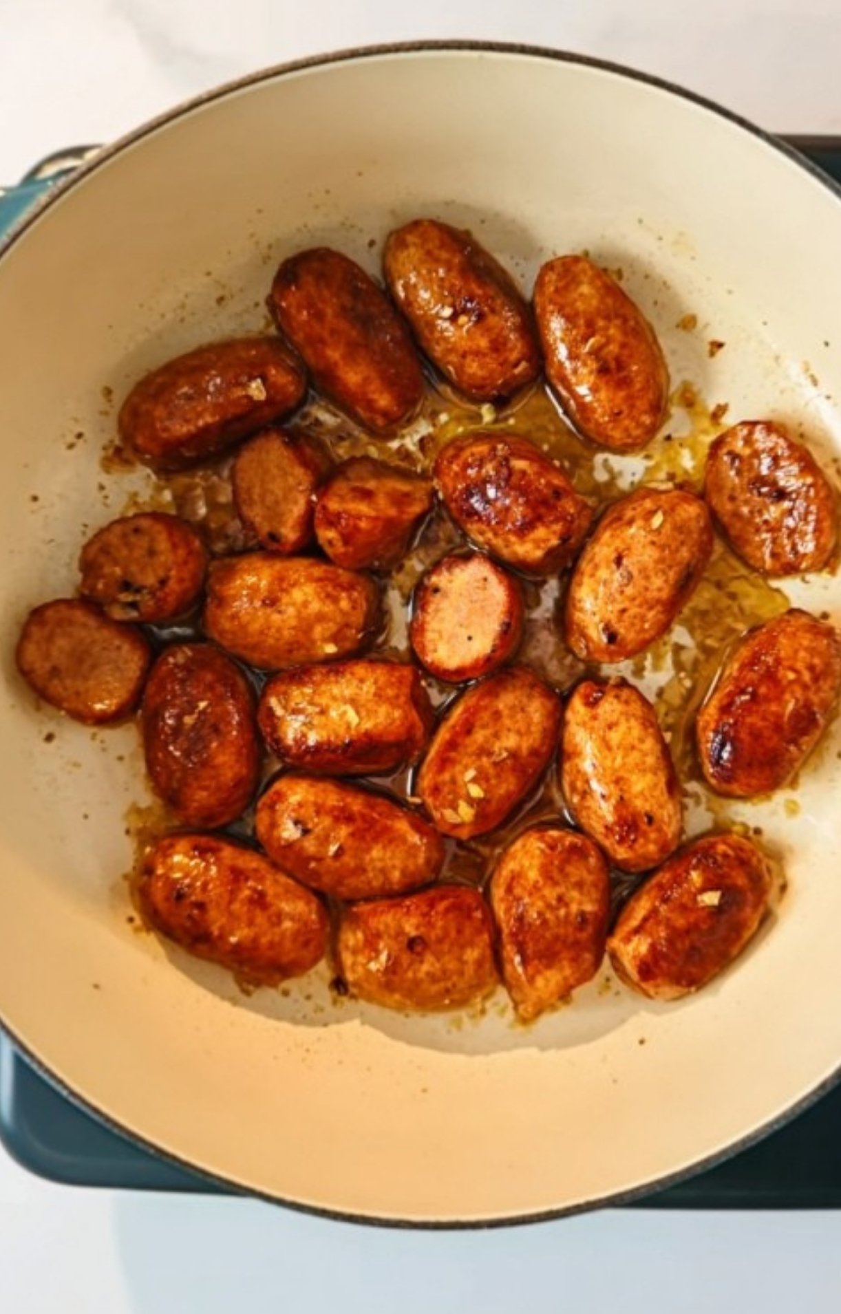 Sliced sausage browning in olive oil inside a Dutch oven, showing an essential step for a classic Chicken Cassoulet.