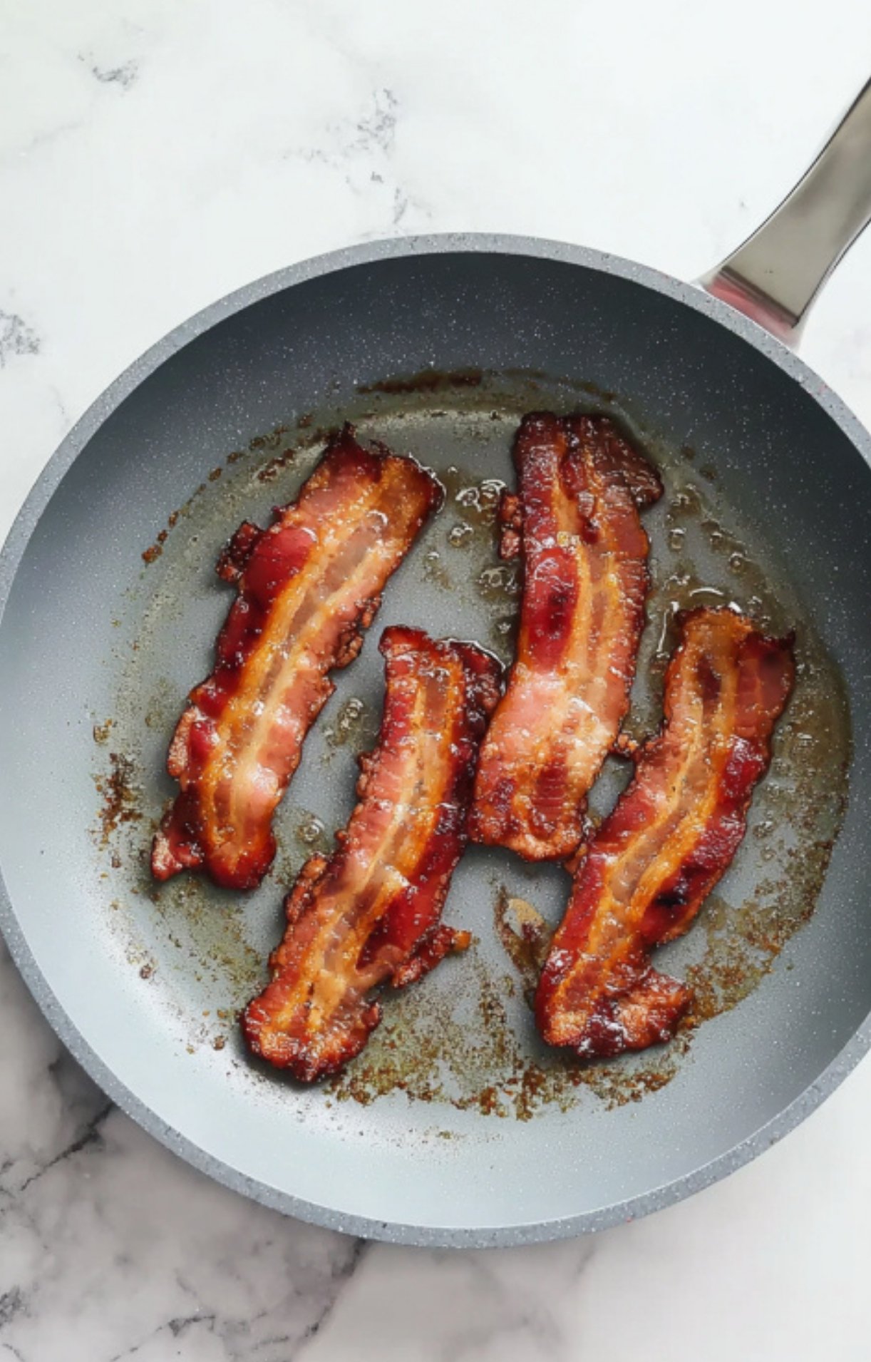 Three strips of crispy bacon in a skillet. Bacon adds smoky flavor and keeps the Beef Wellington extra juicy, a must for comfort food lovers.