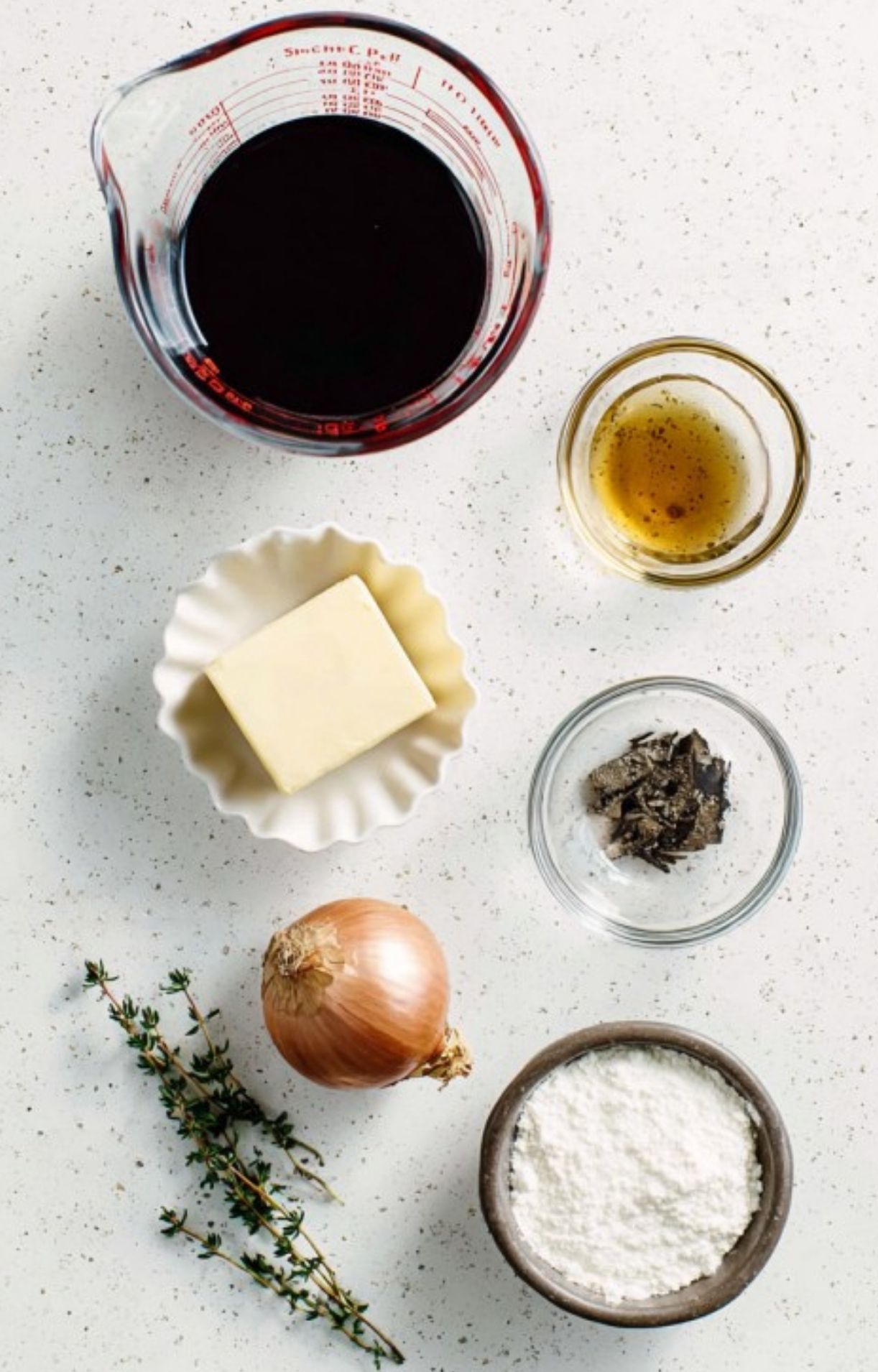 Overhead view of red wine, butter, herbs, onions, and flour—essential ingredients for making homemade red wine sauce for beef wellington.