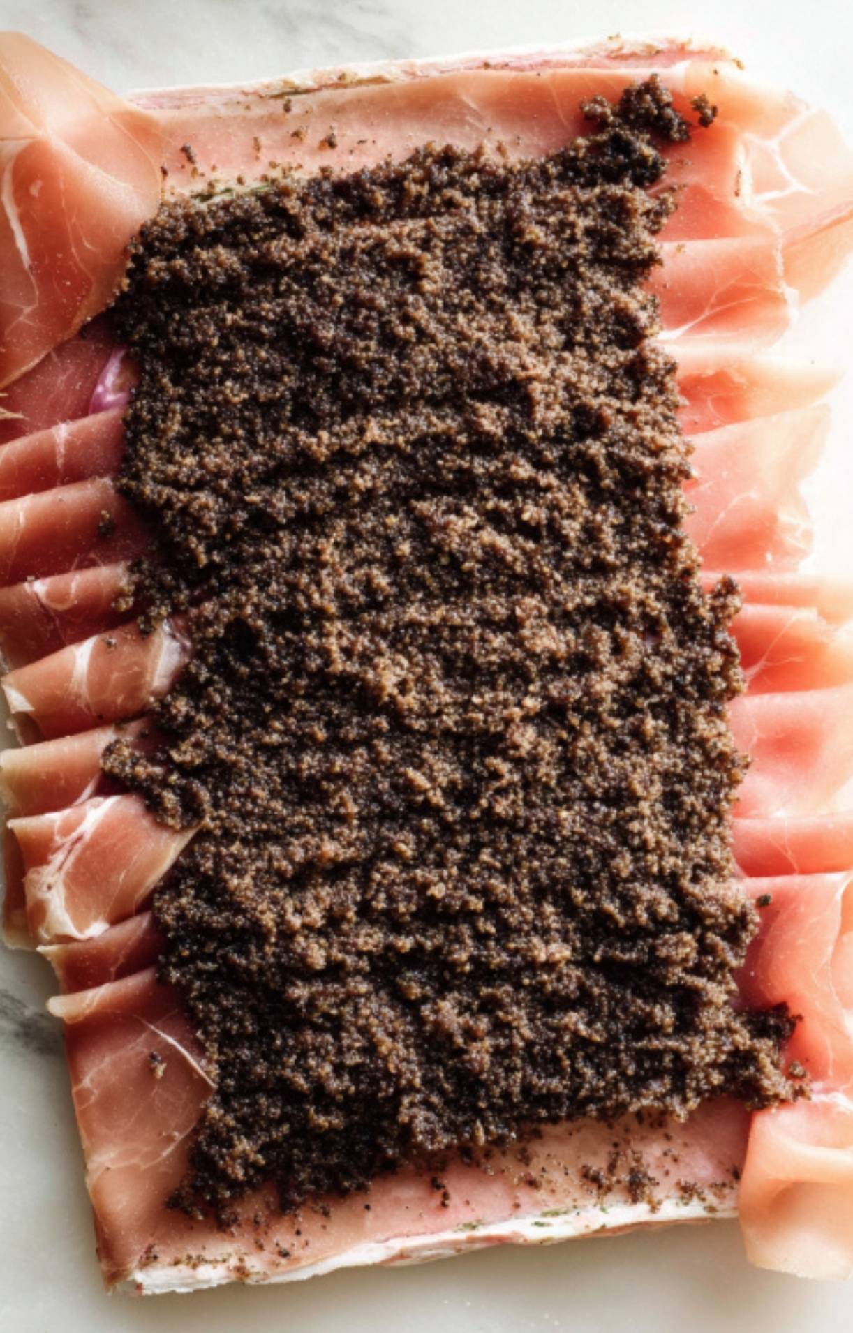 Thin slices of prosciutto topped with a layer of finely chopped mushroom duxelles, ready to wrap around beef tenderloin for beef wellington.