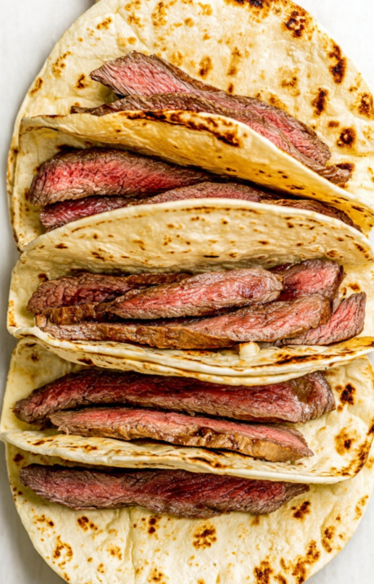 Warm flour tortillas filled with thinly sliced, juicy shaved steak, perfect for quick steak tacos, grilling season, or a cozy weeknight meal.