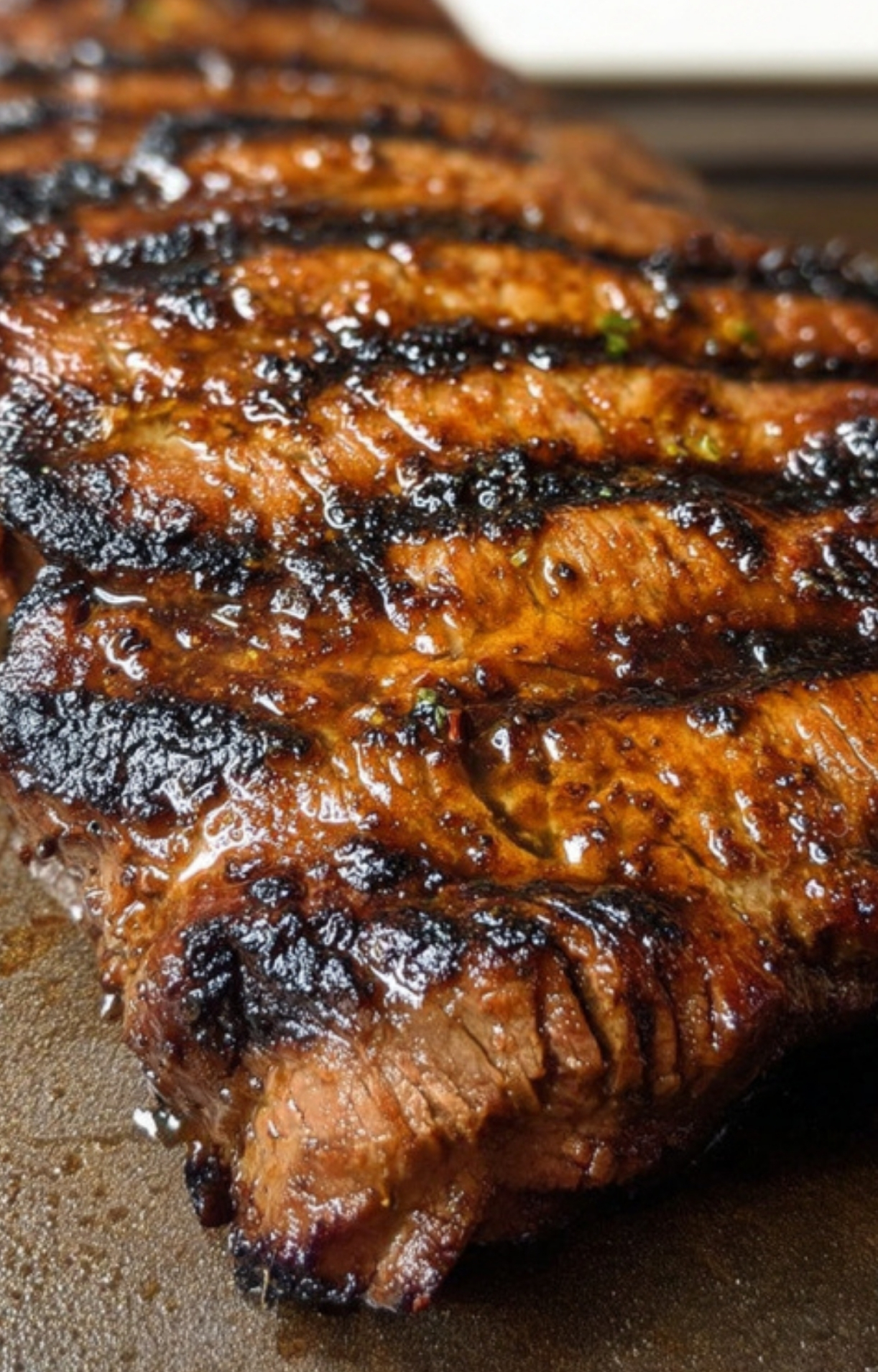 Closeup of juicy marinated flank steak with bold grill marks, showing caramelized edges and a rich glaze, perfect for a summer barbecue or easy weeknight dinner.