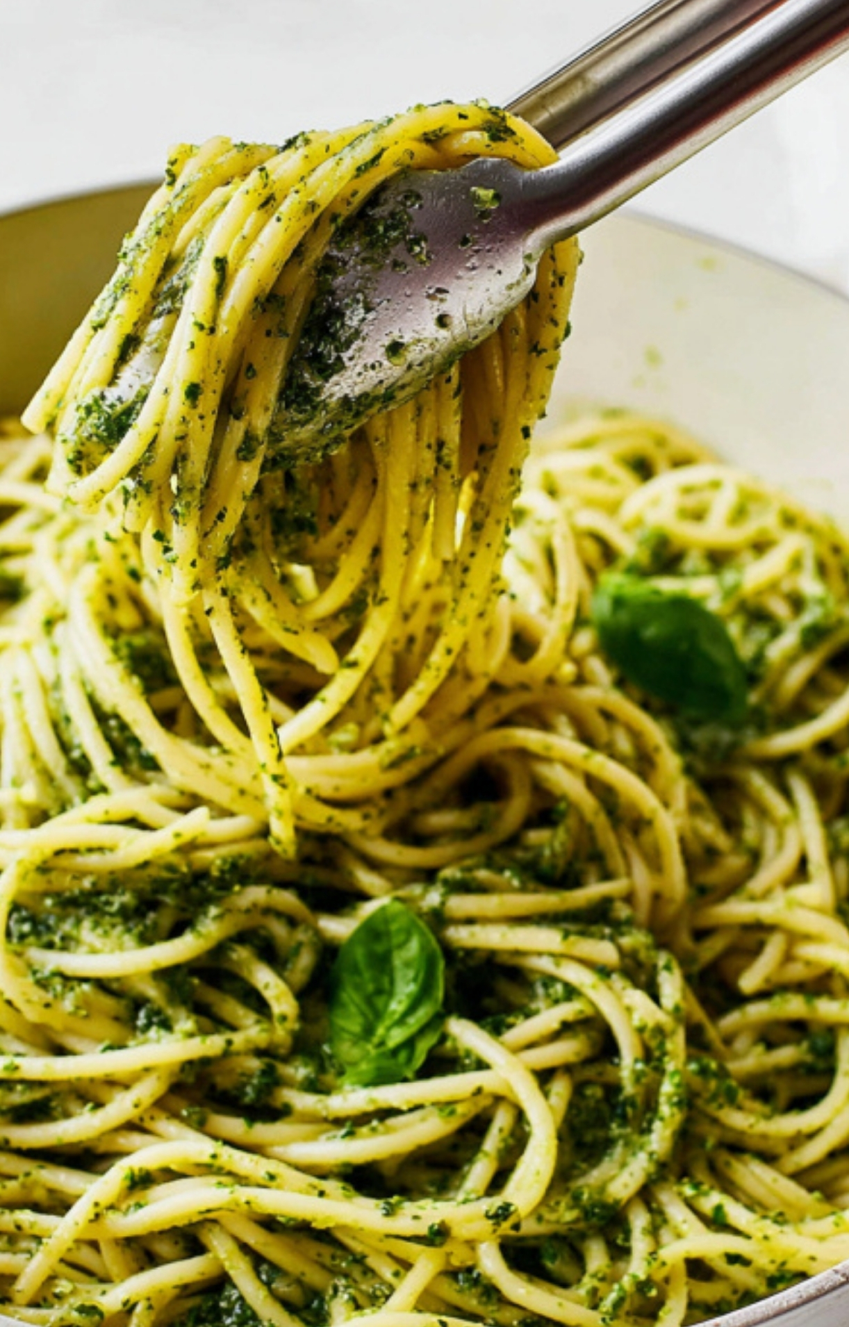 Close-up of spaghetti coated in vibrant basil pesto being twirled with tongs, perfect for an easy week night dinner, Italian comfort food, and fresh, healthy meals.