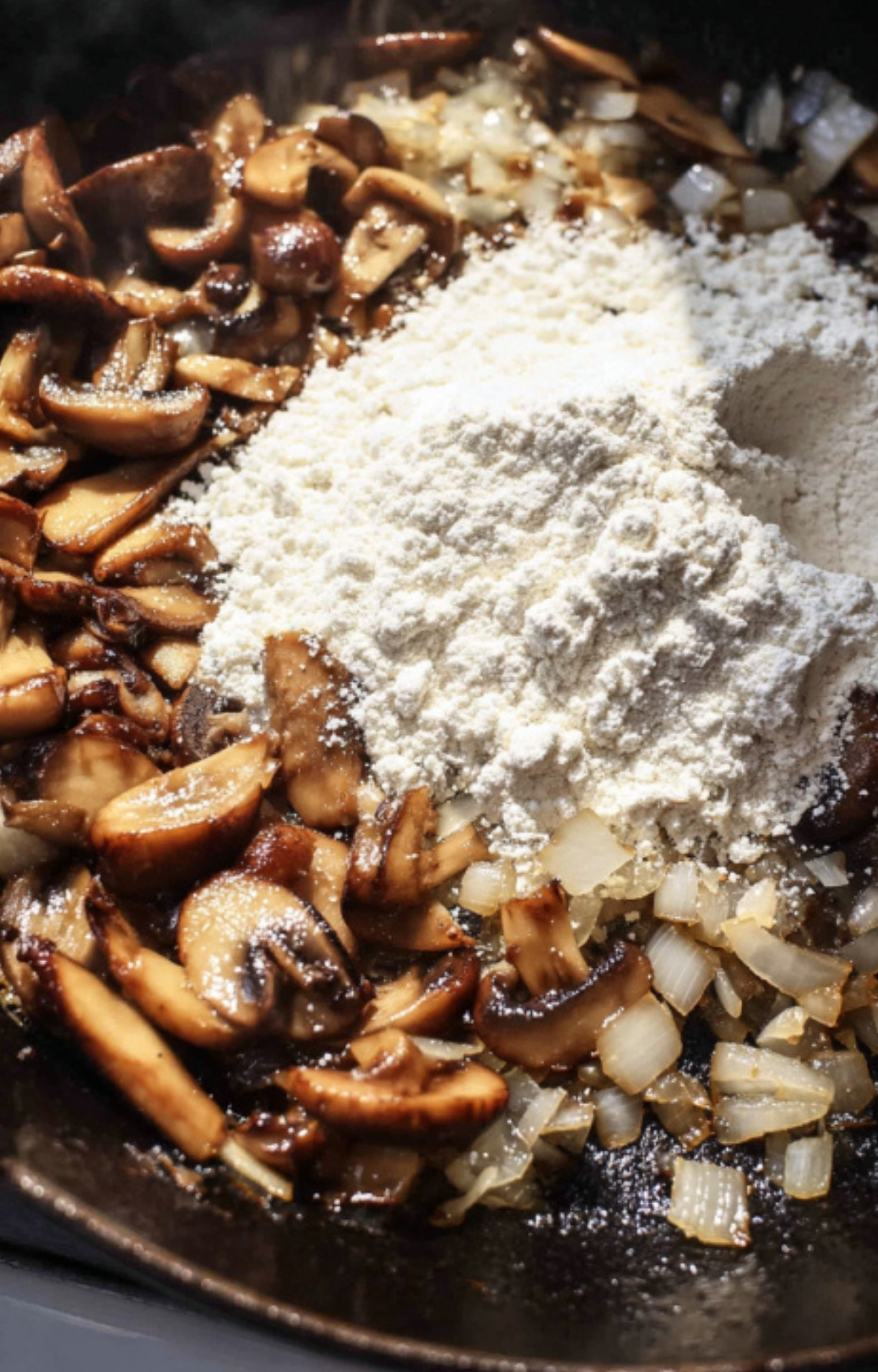 Sliced mushrooms and chopped onions being sautéed with flour in a skillet. Key step for creating a hearty gravy in this classic beef casserole.