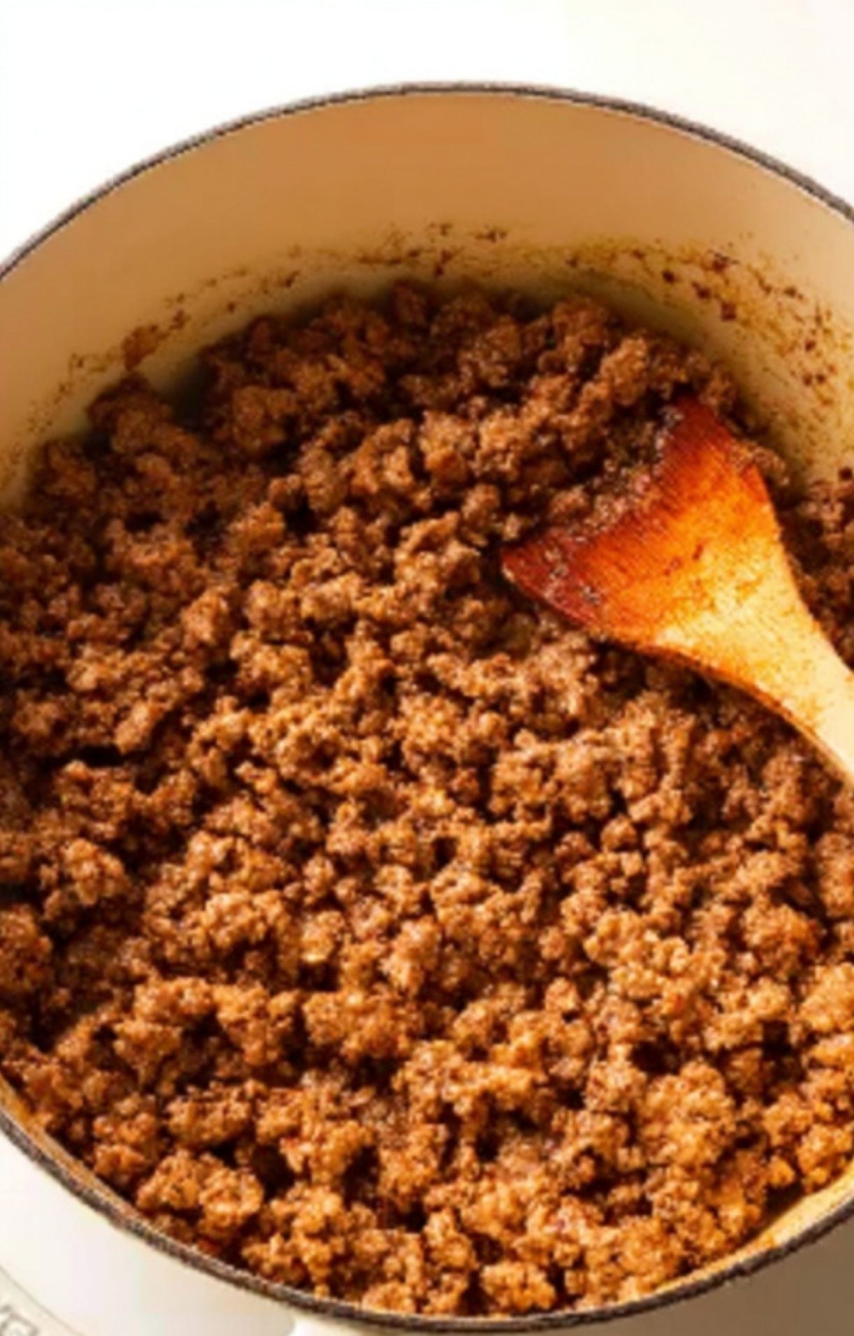 Elbow macaroni being added to a pot of simmering beef and tomato sauce, classic American goulash in the making.