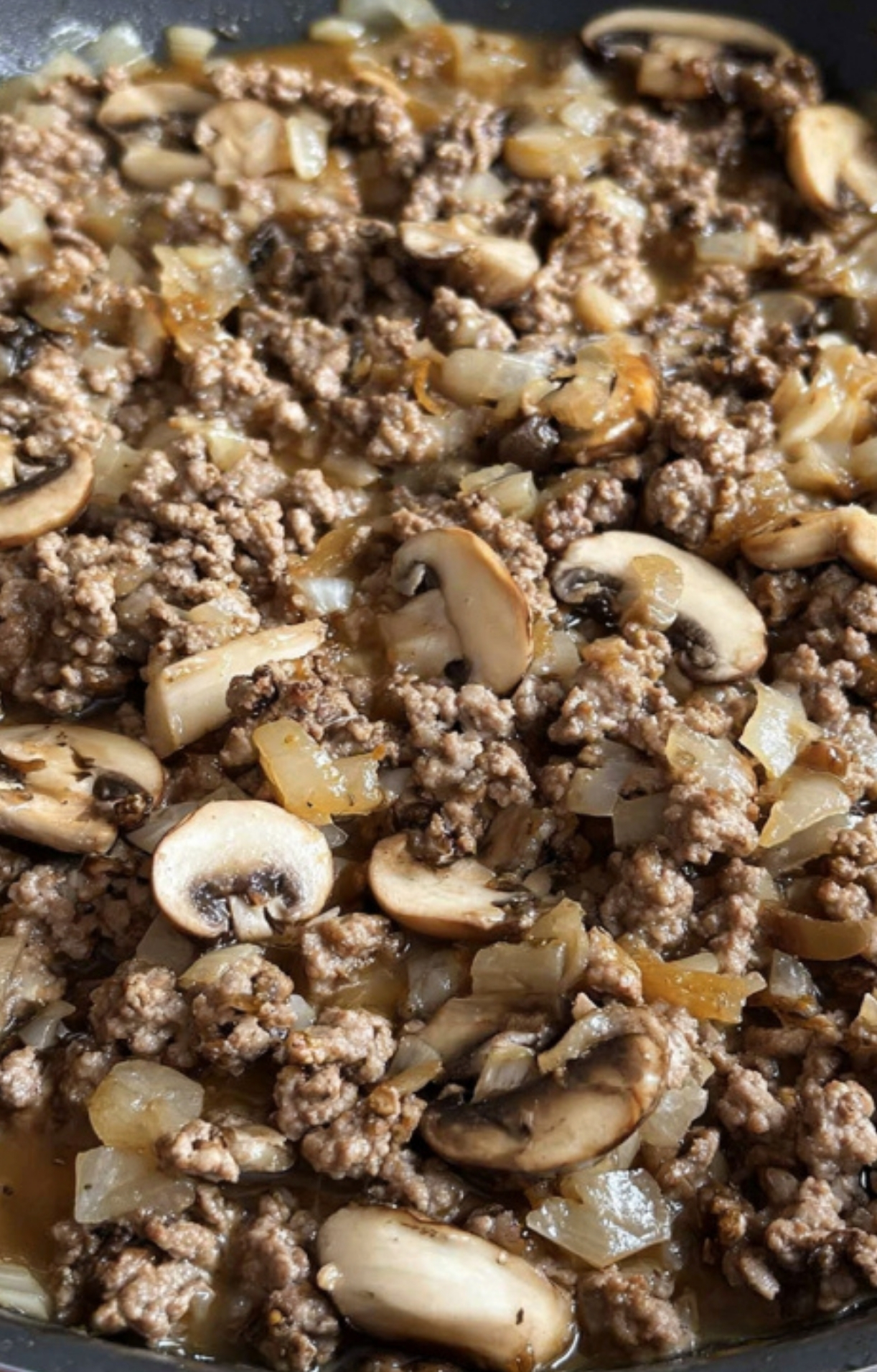 Sliced mushrooms and chopped onions being sautéed with flour in a skillet. Key step for creating a hearty gravy in this classic beef casserole.
