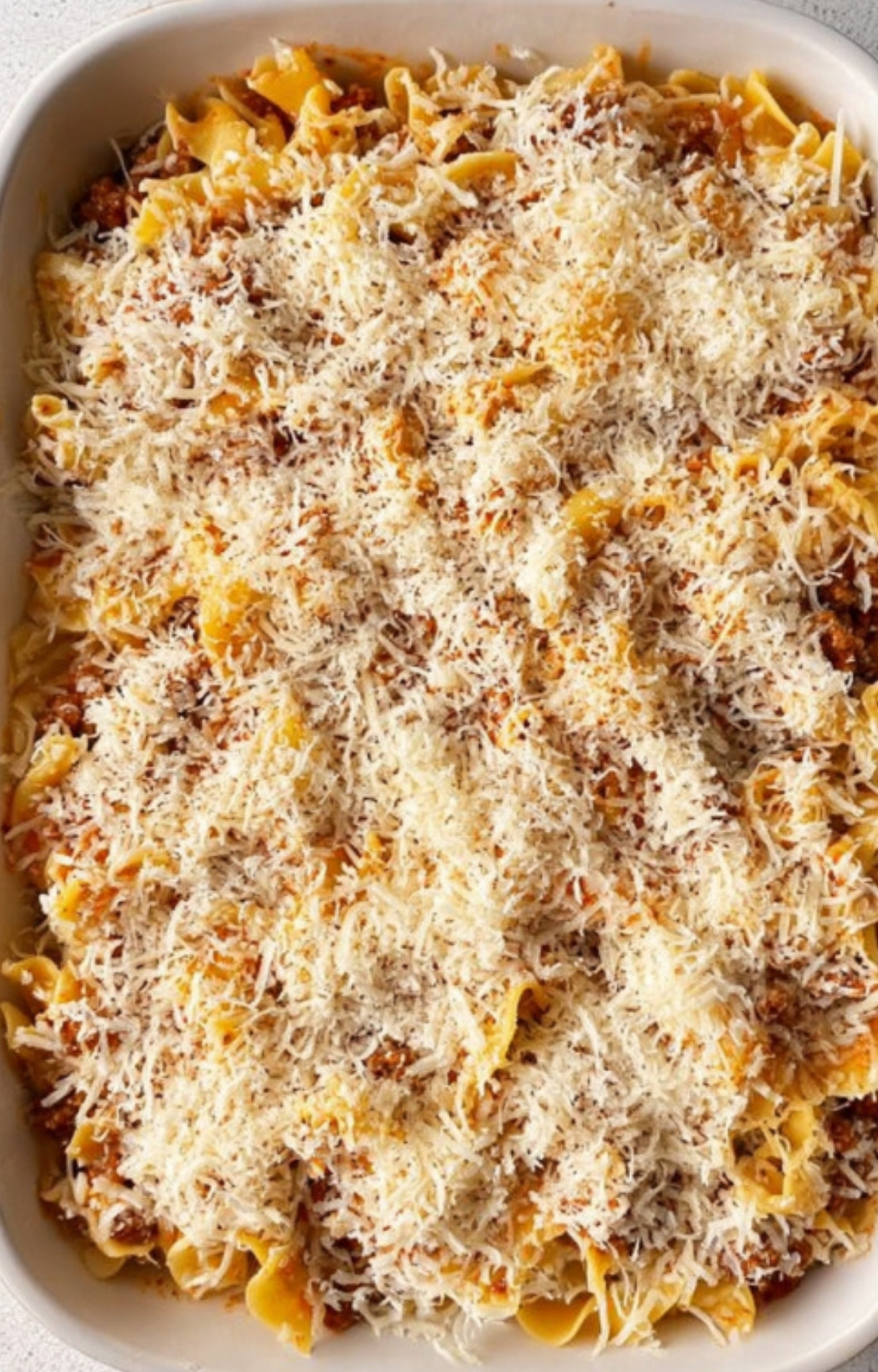 Baked casserole dish filled with egg noodles, ground beef, tomato sauce, and a generous layer of shredded Parmesan cheese, perfect for a cozy family dinner.