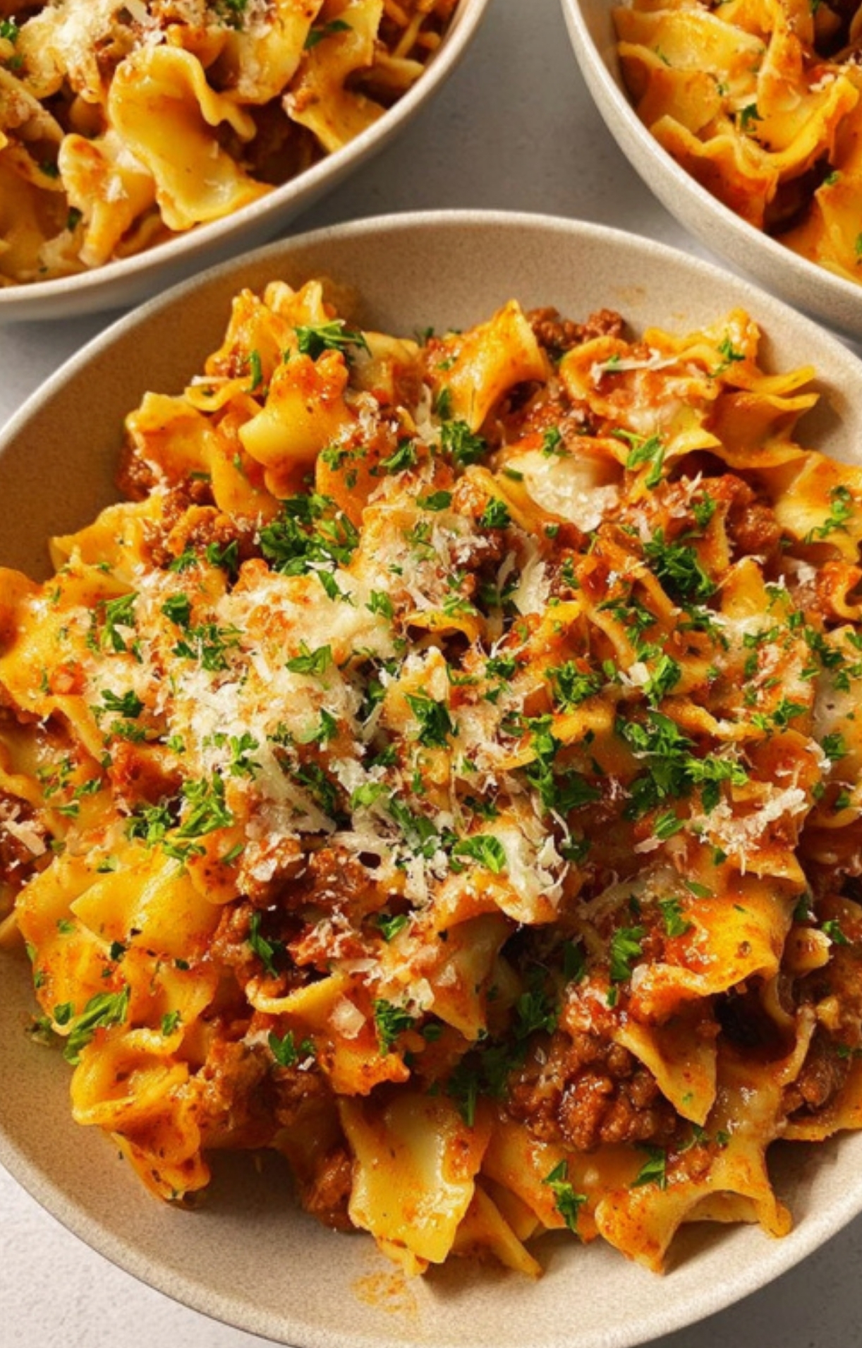 Bowls of quick and easy casserole with wide noodles, ground beef sauce, melty cheese, and fresh parsley, served hot for a family dinner.