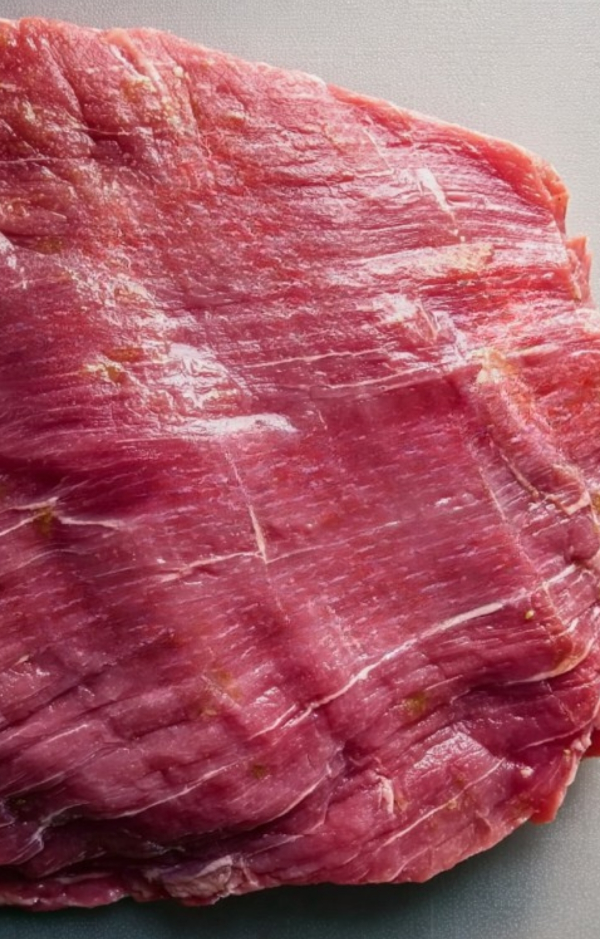 Uncooked flank steak laid out on a cutting board, showing lean marbling and perfect texture for grilling.