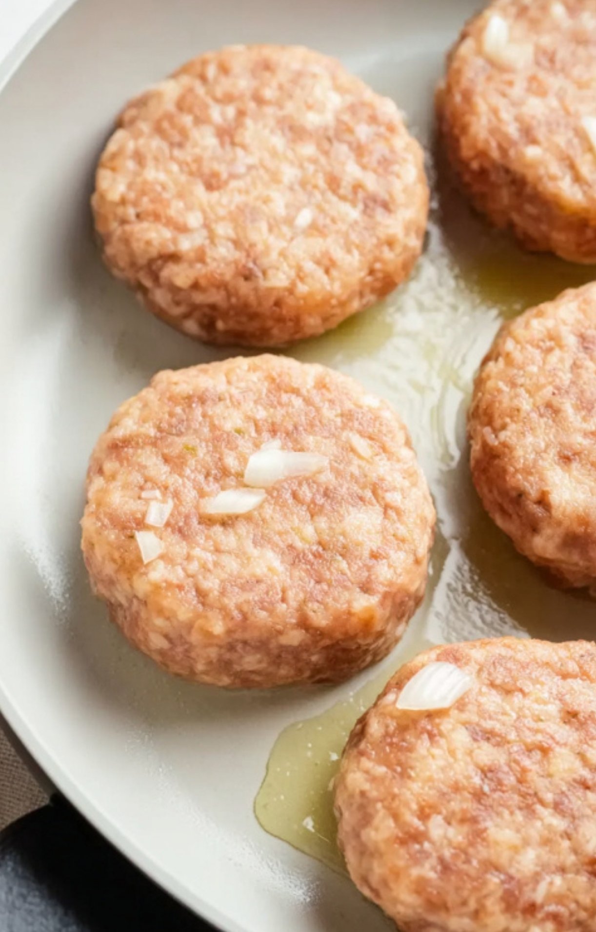 Raw ground turkey Salisbury steak patties with diced onions resting in a lightly oiled skillet before cooking.