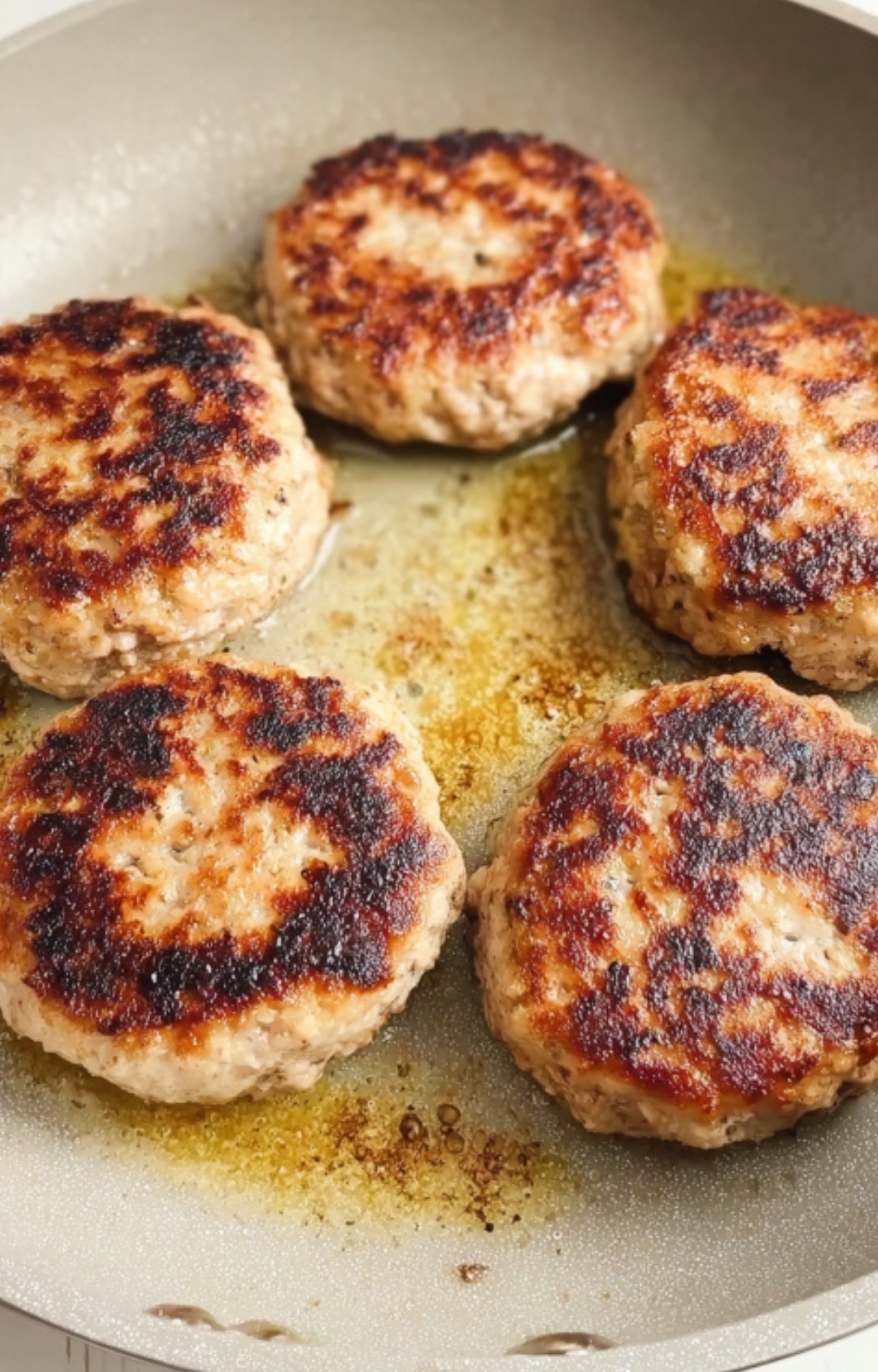 Golden-brown ground turkey Salisbury steak patties sizzling in a skillet during the searing process.