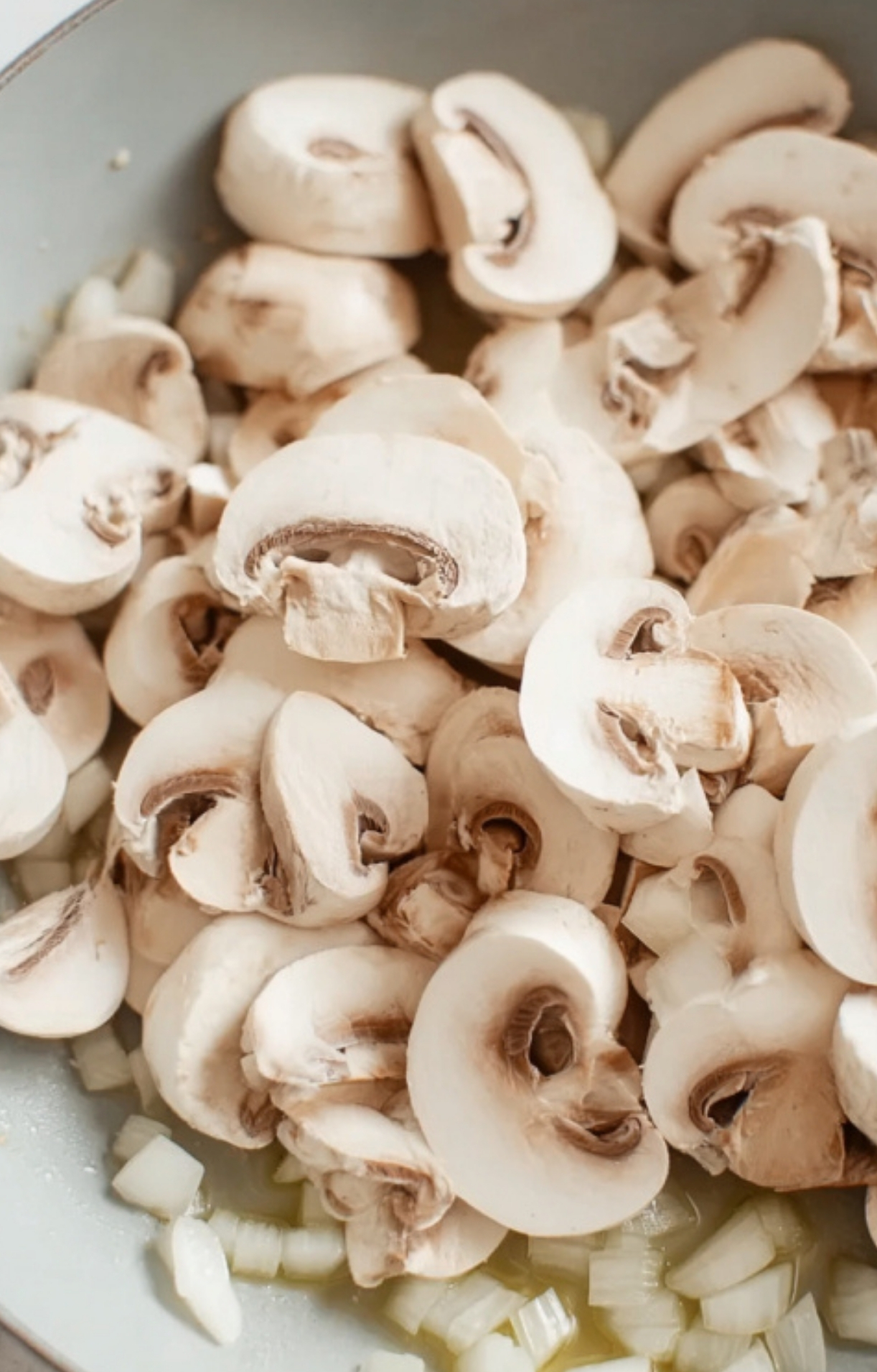 Sliced fresh mushrooms added to a skillet with diced onions before cooking for Salisbury steak gravy.