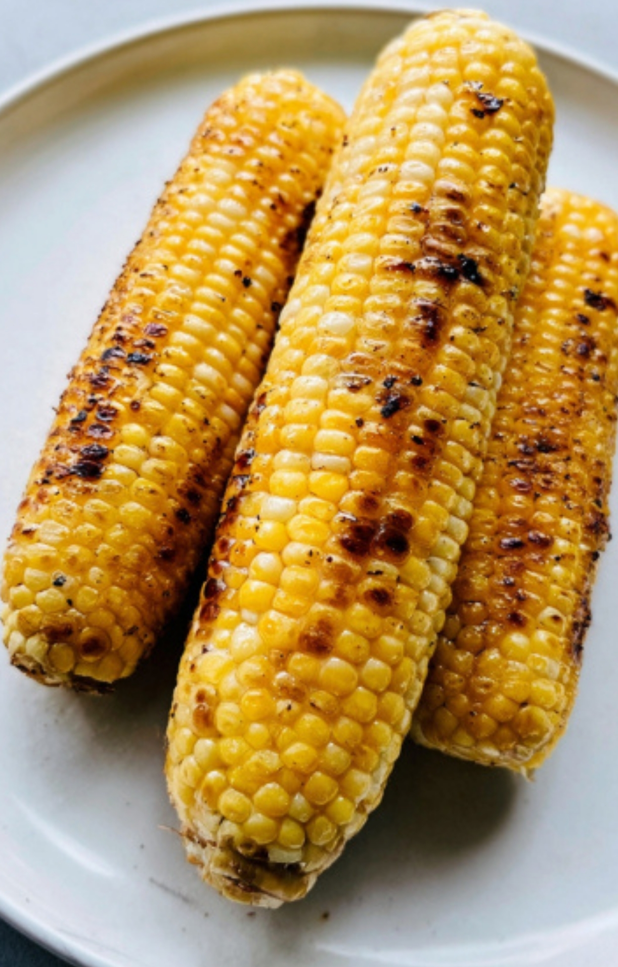 Three ears of grilled corn on a plate, perfect for making fresh salsa or serving with steak.