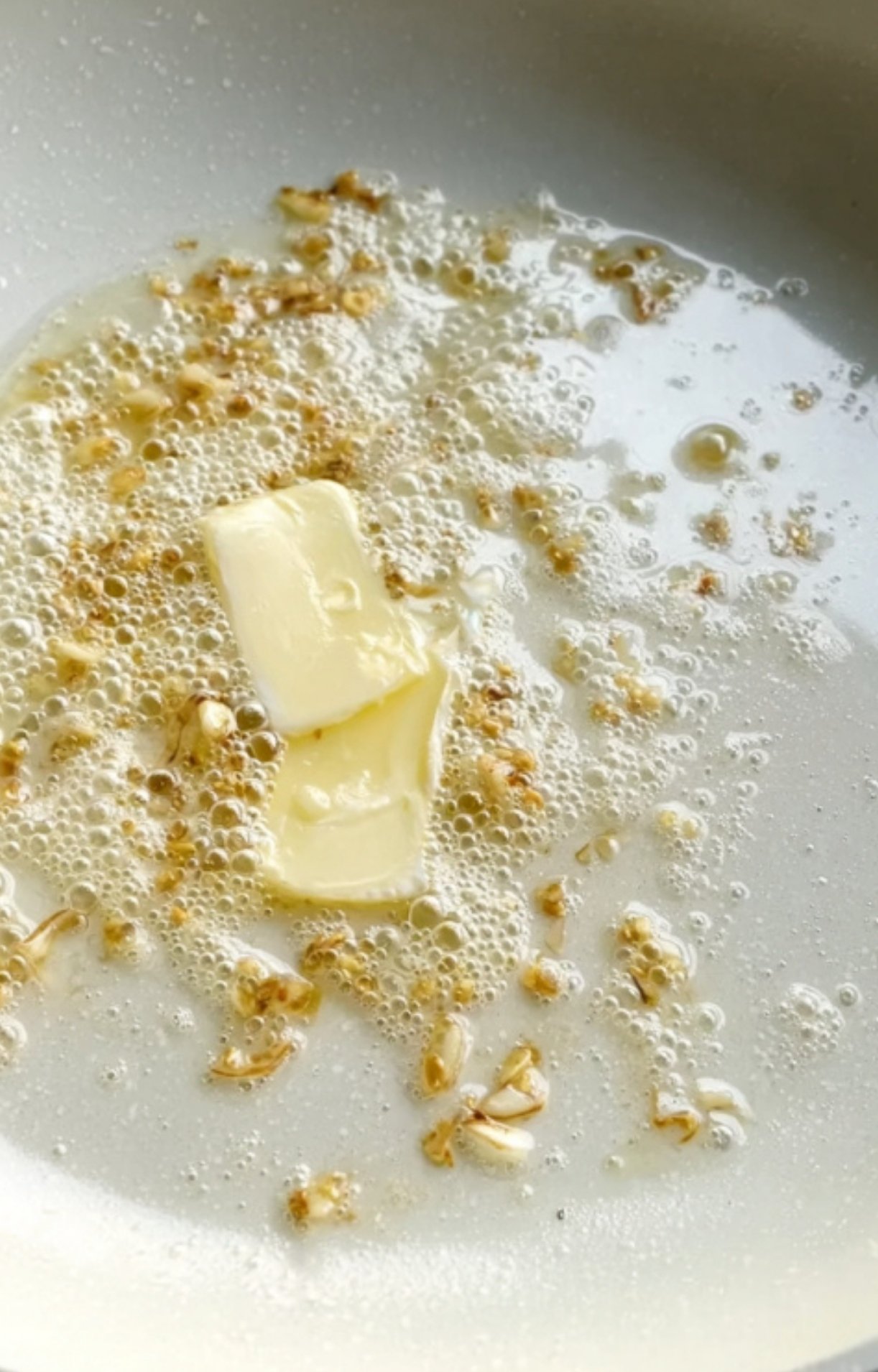 Butter melting in a skillet with golden sautéed garlic as the first step of making gravy.