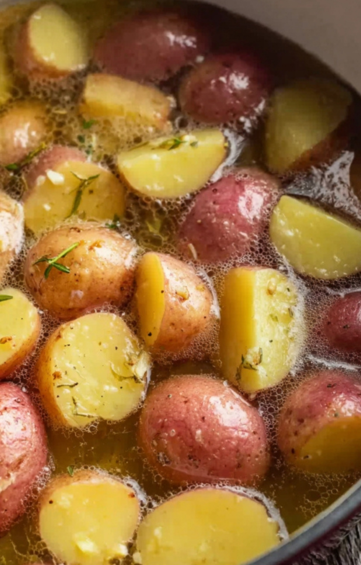 Baby red potatoes simmering in a pot with herbs, getting ready for a cheesy ranch potato casserole recipe.