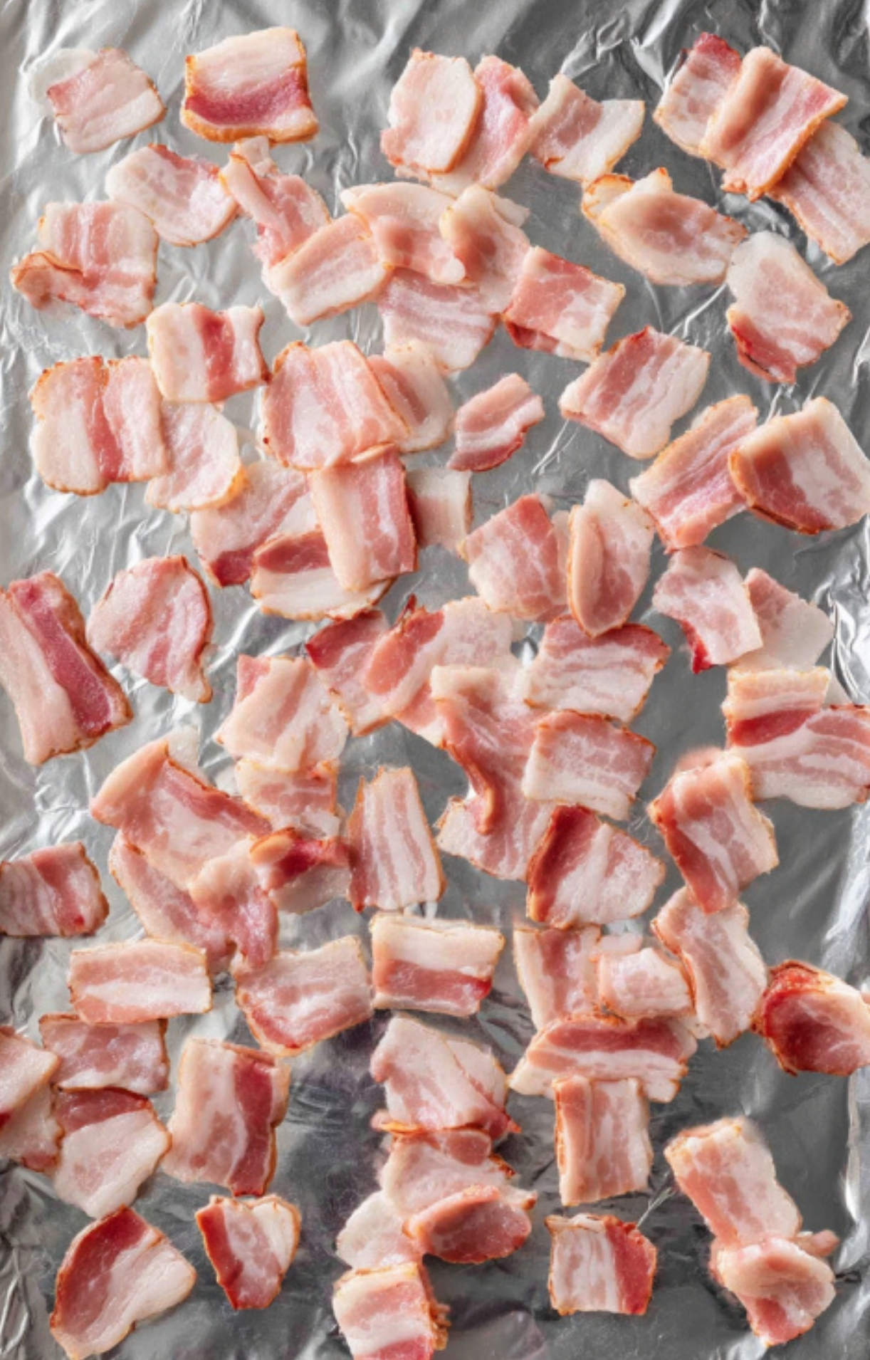 Sheet pan lined with foil and chopped bacon, prepared for baking in the cheesy bacon ranch potatoes recipe.